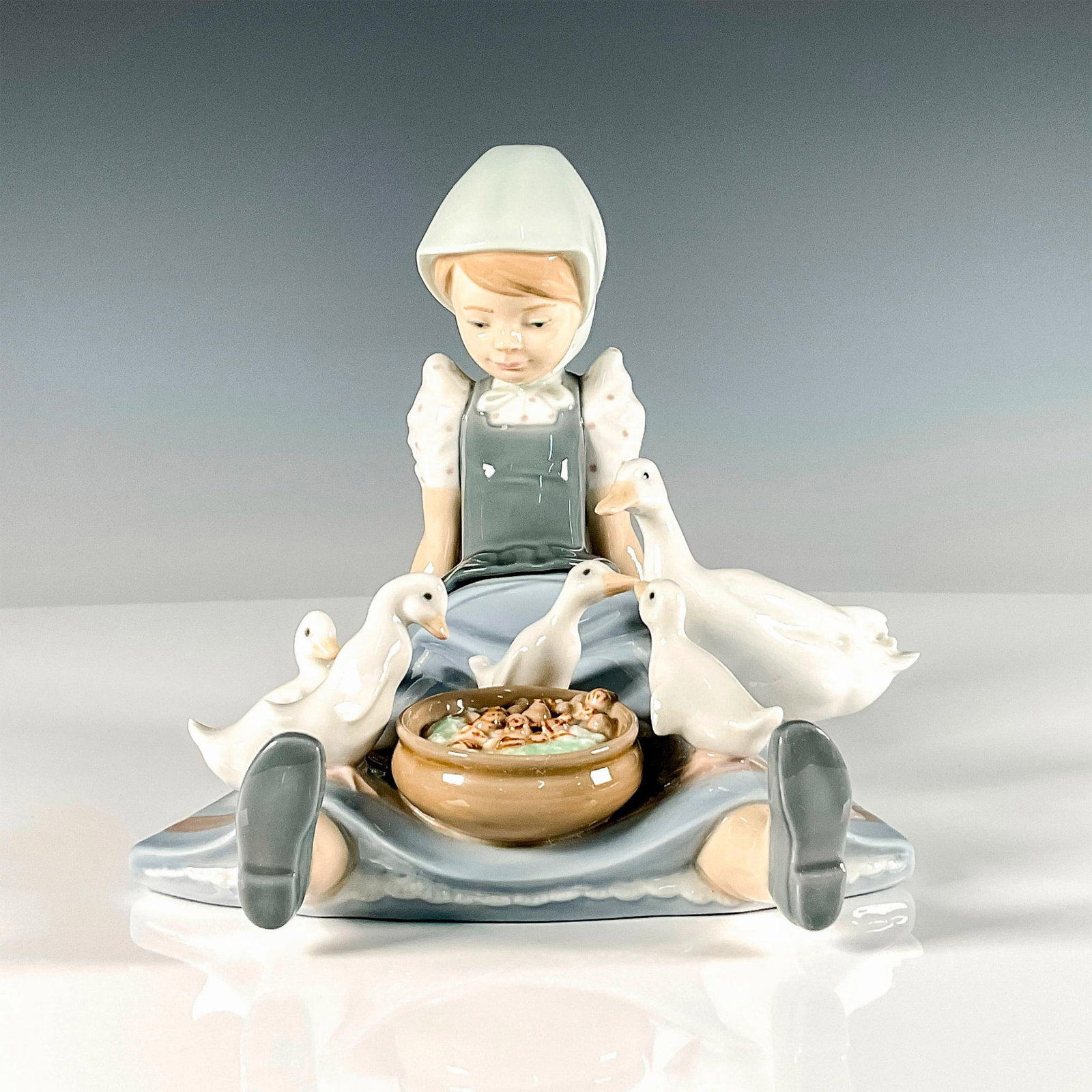 My Hungry Brood 1005074 - Lladro Porcelain Figurine: Glossy finish; young village girl feeding her ducklings. Lladro backstamp. Artist: Juan Huerta Issued: 1980-1997 Dimensions: 6.25"L x 8"W x 6.75"H Manufacturer: Lladro Country of Origin: Spain