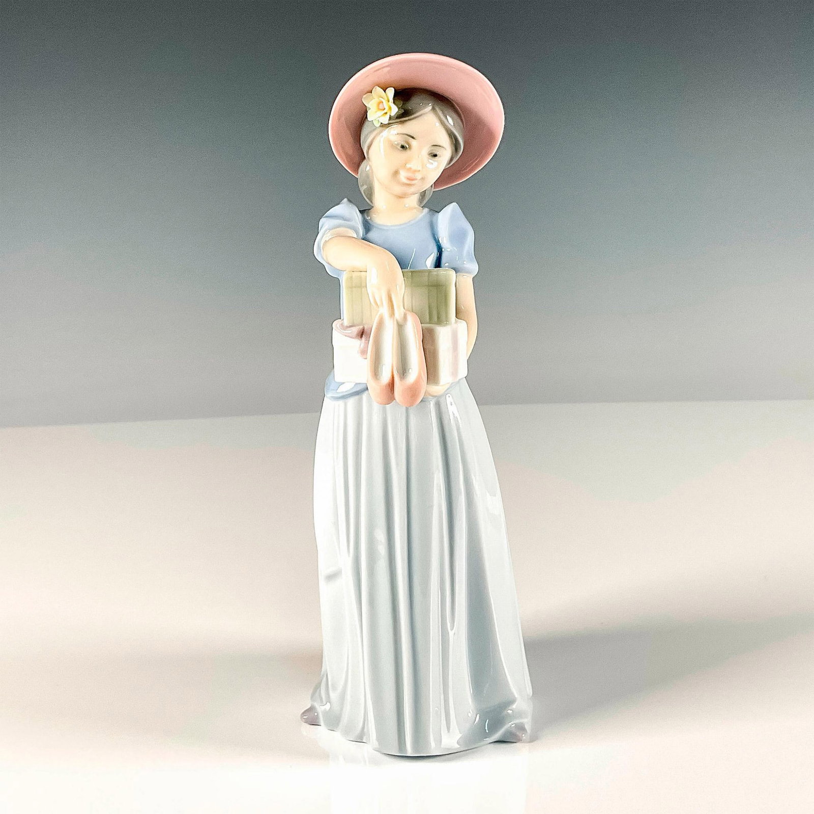 New Shoes 1006487 - Lladro Porcelain Figurine: Glossy finish figure of girl holding the boxes of shoes she just received. Lladro backstamp. Artist: Marco Antonio Nogueron Issued: 1998-2001 Dimensions: 3"L x 3.25"W x 8"H Manufacturer: Lladro Count