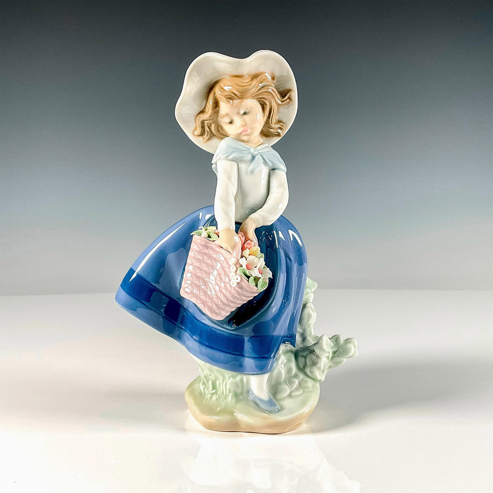 Pretty Pickings 1005222 - Lladro Porcelain Figurine: Glossy finish figure of a young girl holding a basket of flowers. Lladro backstamp. Artist: Jose Puche Issued: 1984 Dimensions: 5"L x 4"W x 7.25"H Manufacturer: Lladro Country of Origin: Spain