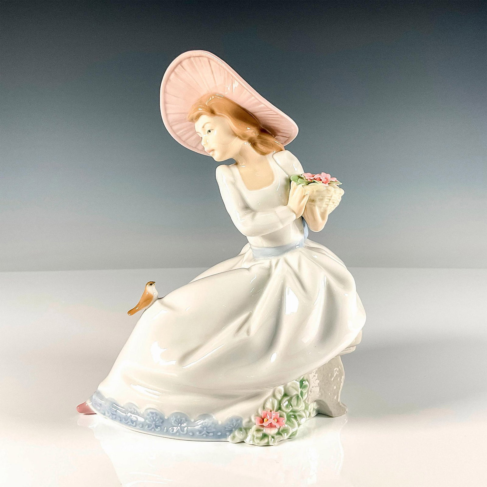 The Nightingale's Song - Nao By Lladro Porcelain Figurine: Glossy finish lovely figure featuring a young lady sitting peacefully arranging the basket of fresh flowers she just picked while a delicate nightingale sits on her lap. Nao By Lladro backstamp. Artis
