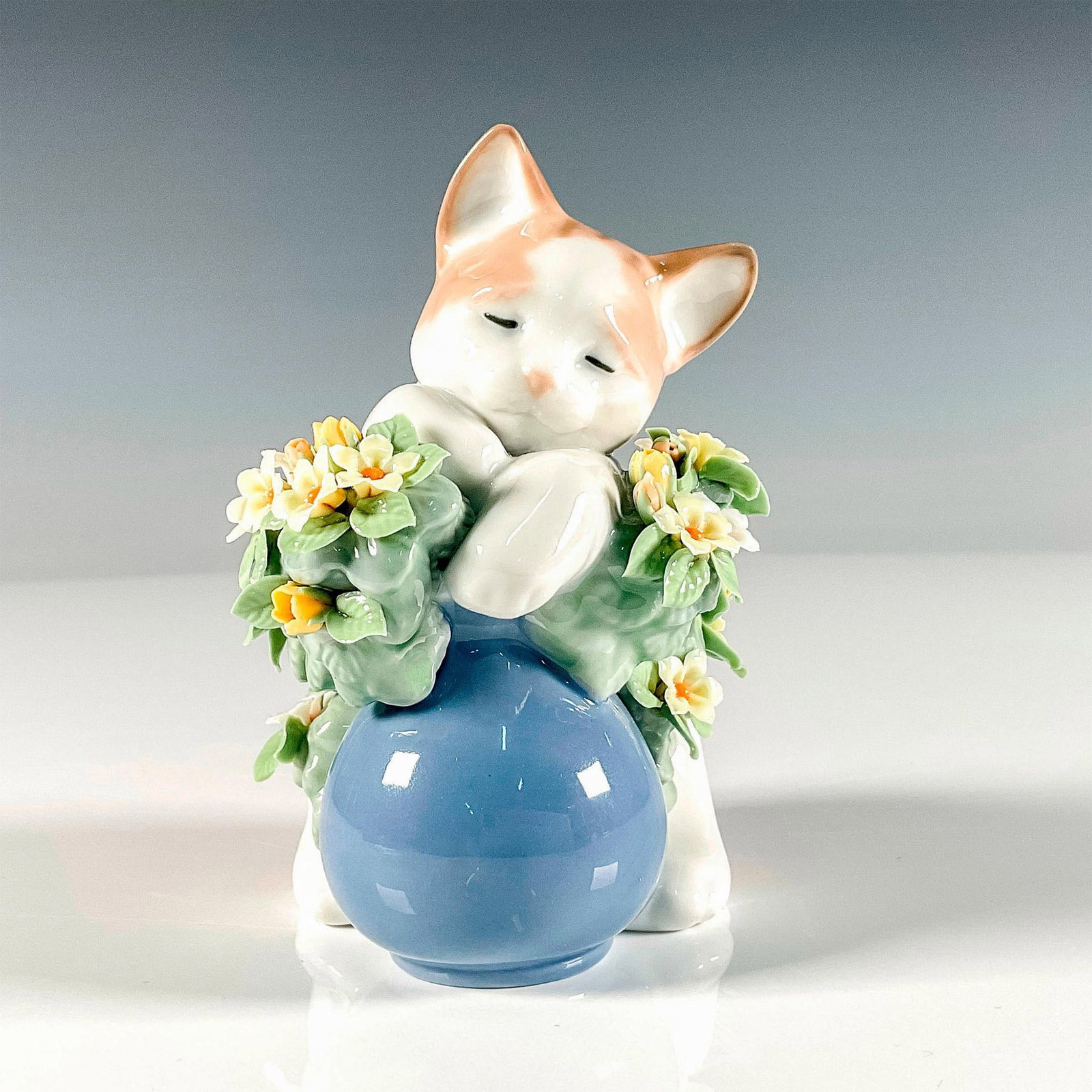 Dreamy Kitten 1006567 - Lladro Porcelain Figurine: Glossy finish charming figure depicting a cute cat resting on a pot of delicate flowers. Lladro backstamp. Artist: Juan Huerta Issued: 1999 Dimensions: 2.75"L x 3.5"W x 4.25"H Manufacturer: Lladro Co