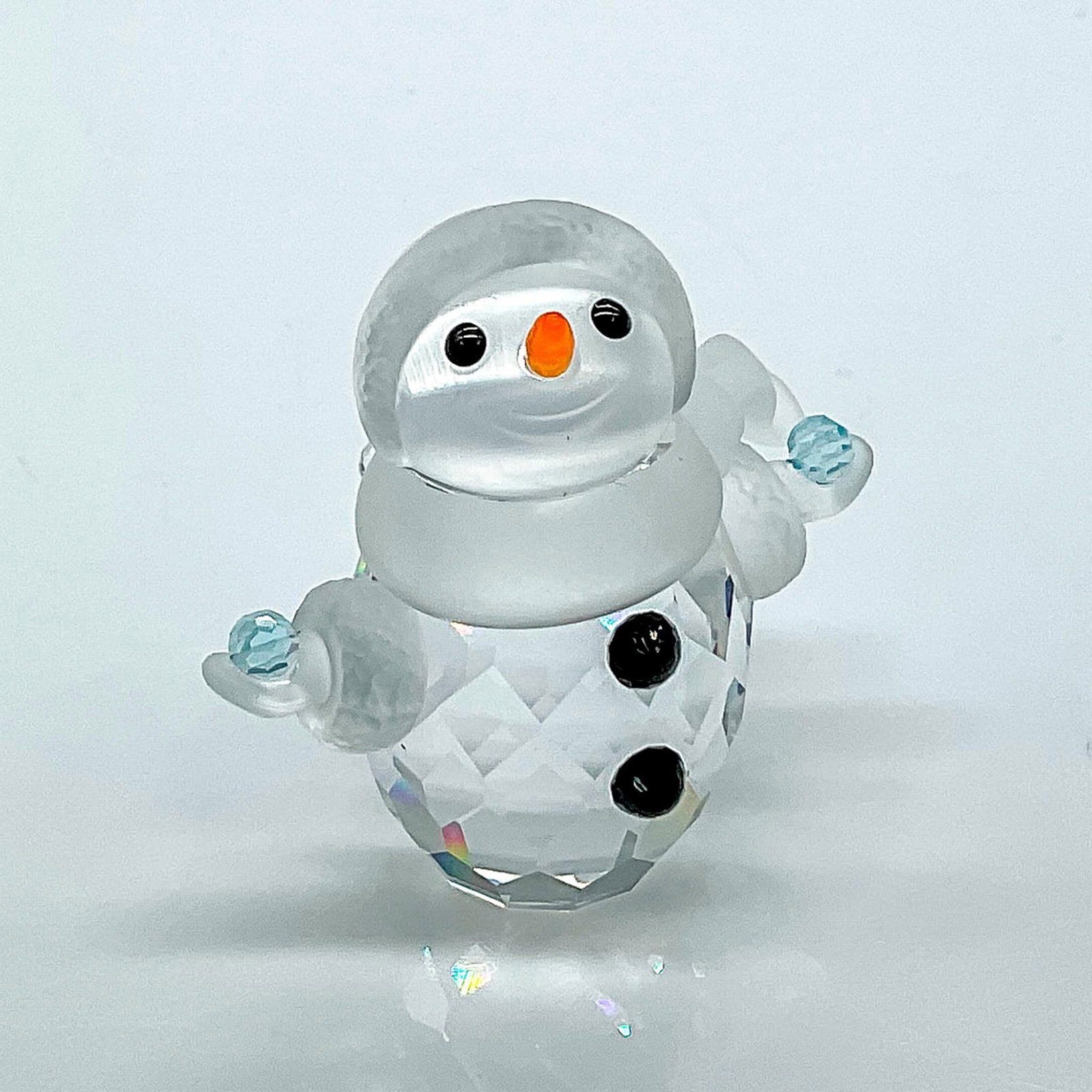 Swarovski Crystal Figurine, Snowman: Multifaceted clear crystal with black eyes and buttons, orange carrot nose, frosted scarf and hat rim, and mittens with a pale blue snowball in each hand. Part of the Cheerful Times collection. Swarov