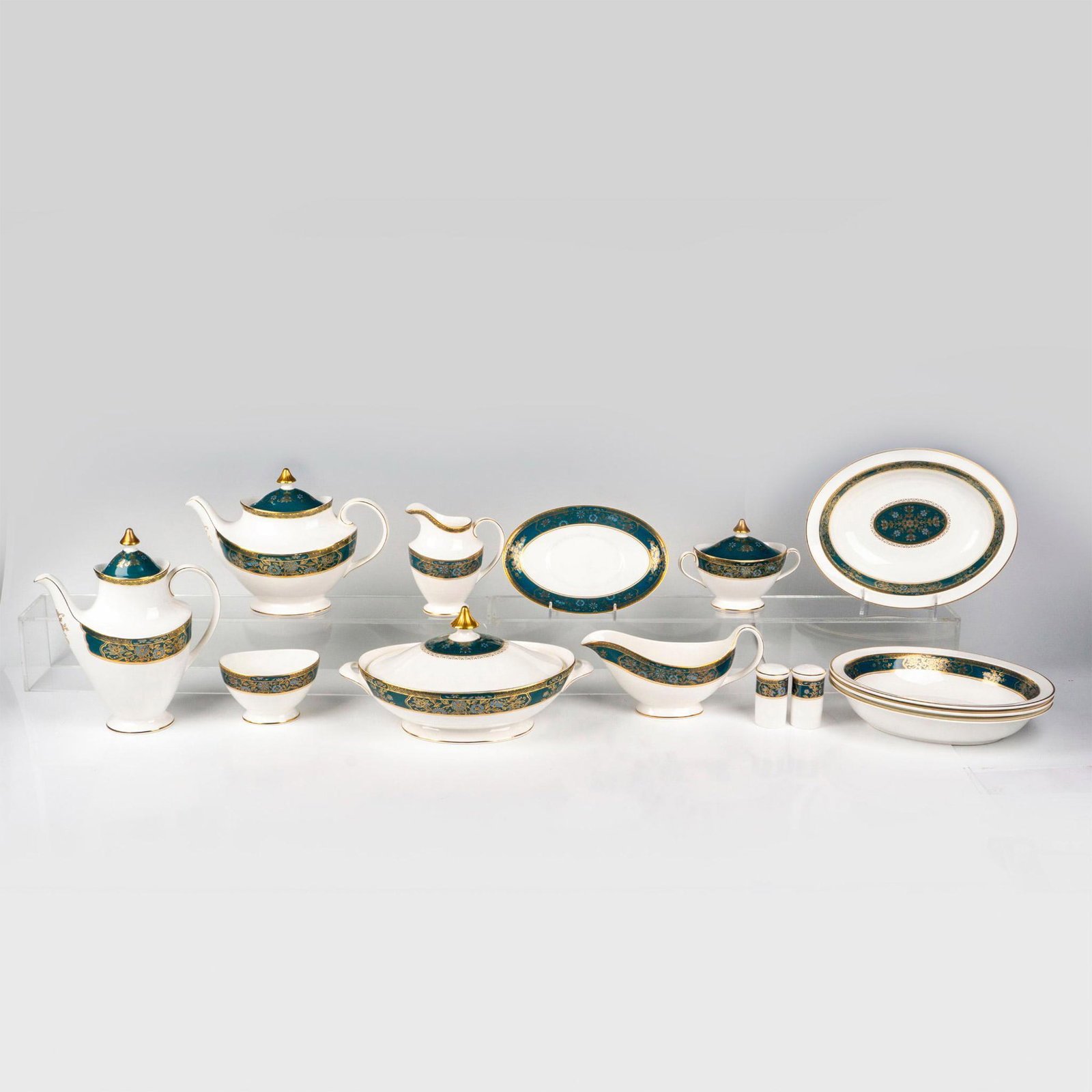 14pc Royal Doulton Bone China Serveware, Carlyle: Fourteen tableware serving items in white with a blue floral and gold design on dark deal. Royal Doulton backstamp. Teapot 10.5"L x 5.5"W x 7.5"H. Coffee pot 9"L x 4.25"W x 10"H. Four oval serving dis