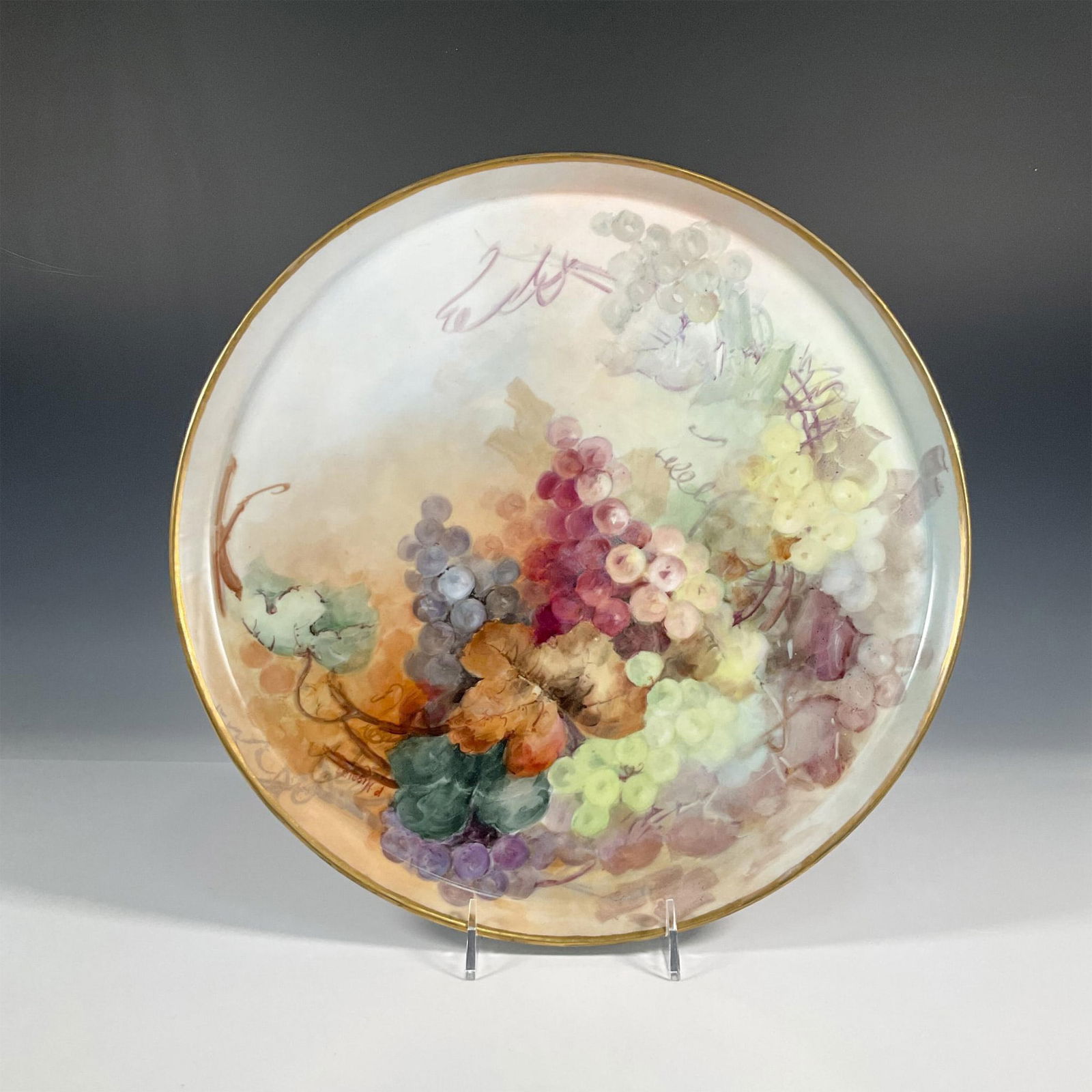 Tressemanes & Vogt Higgins Porcelain Limoges Tray: A large round centerpiece tray with a gilded trim and hand painted grapes. Tressemanes & Vogt backstamp. Artist signed on the front. Artist: P. Higgins Issued: 1919-1928 Dimensions: 15.75"W x 0.75"H M