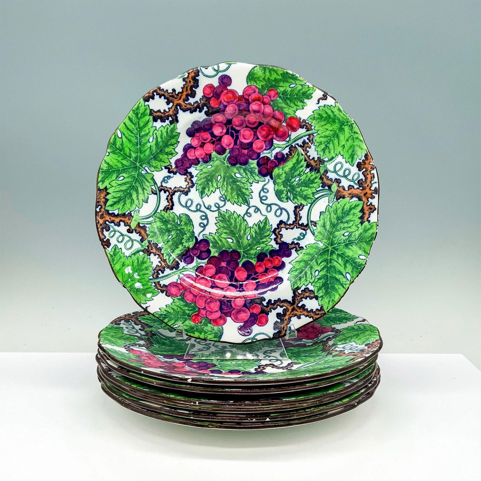 7pc Copeland Spode Grape Motif Plates: A set of 7 identical white plates with wavy borders that have a design of grape and grapevines taking over the plate. Copeland Spode backstamp. Soane and Smith backstamp. Dimensions: 9"H x 0.75" dia.