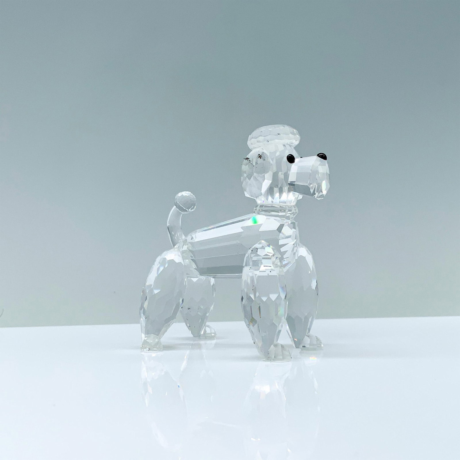 Swarovski Crystal Figurine, Standing Poodle: A clear crystal figurine of a well-groomed poodle with a fluffy head and tail standing on all fours. Swarovski backstamp. This item has its original box. Dimensions of the original box: 3.75"H x 5" di