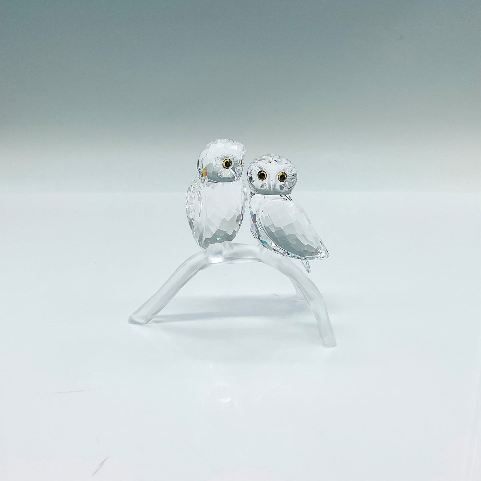 Swarovski Crystal Figurine, Pair of Owls on Branch Signed: Sparkling cut crystal figure of two owls with yellow crystal eyes perched on a branch. Swarovski etched mark. Artist signed. This item has its original box: 6"L x 6"W x 3.75"H. Artist: Anton Hirzinger