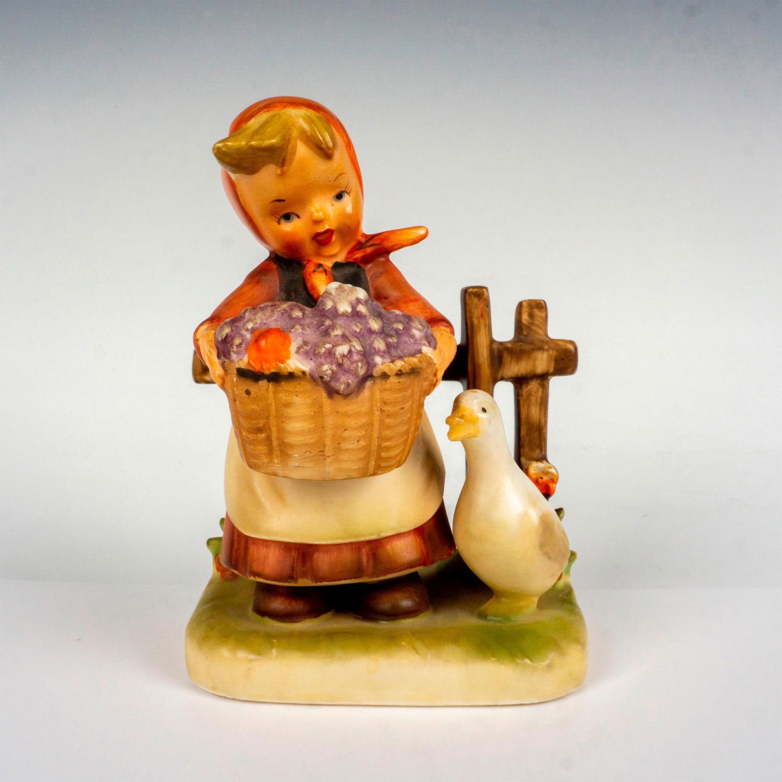 Erich Stauffer Porcelain Farm Girl Figurine: Hand painted in matte finish figurine in the style of Goebel-Hummel. This cute figure depicts a farm girl carrying basket full of grapes while a goose guards her by her side. Designed by Erich Stauffe