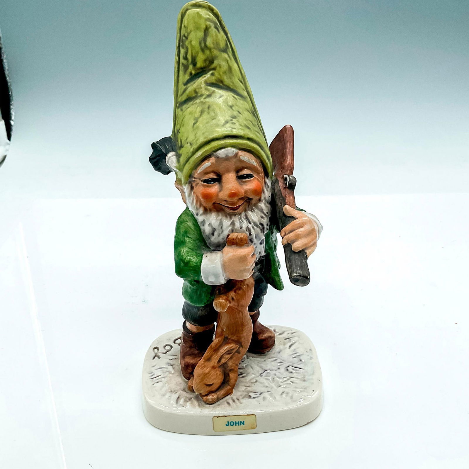 Goebel Hummel Porcelain Figurine, John Hawkey the Hunter: Hand painted gnome with green hat, rifle and rabbit. Goebel Hummel W Germany backstamp. Impress mark Well518. Issued: 20th century Dimensions: 3.5"L x 3.25"W x 7"H Manufacturer: Goebel Hummel Country