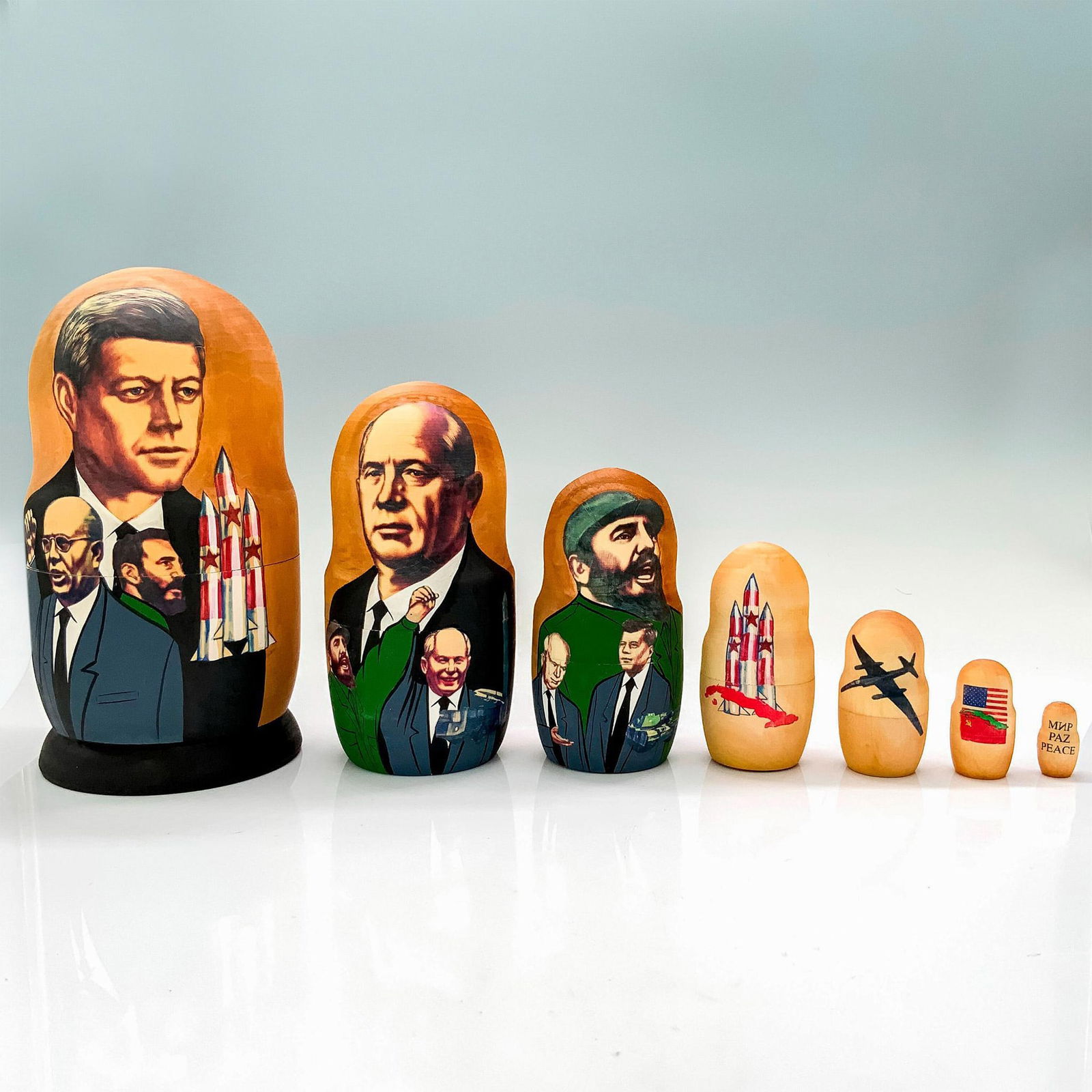 Nesting Dolls, John F Kennedy 1960's Motif: A set of 7 nesting dolls depicting the 1960's through figureheads and moments of that time. Dimensions of the largest nesting doll: 8"H x 4" dia. Dimensions: 8"H x 4" dia. Edition Number: 357/500