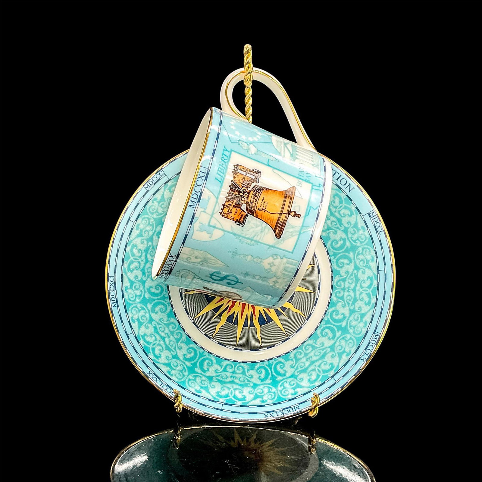 3pc Wedgwood Cups/Saucers/Stands, Millennium Collection: Bone china tea cup and saucer. Cup with detailed images representing particular historical memorabilia, gold rims. Saucer with spirited image of the sun. Wedgwood backstamp. Cup 4.25"L x 3.25"W x 2.25