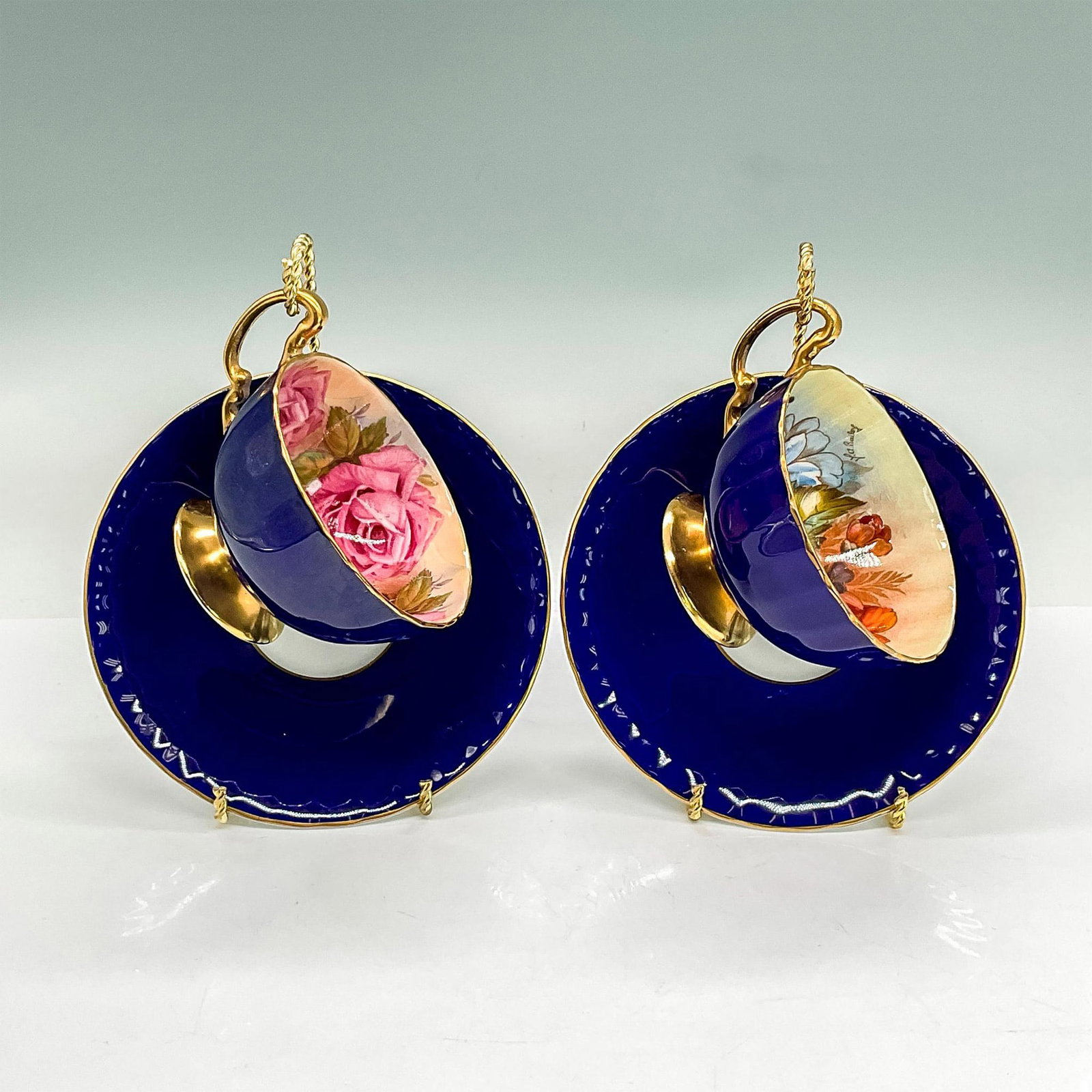 6pc Aynsley China Teacups/Saucers/Stands: Bone china tea cups and saucers. Two cups in dark blue with floral interiors, gold rims. Two saucers in cobalt blue with white center. Aynsley backstamp. Cups 4.5"L x 3.5"W x 2.25"H. Saucers 0.75"H x