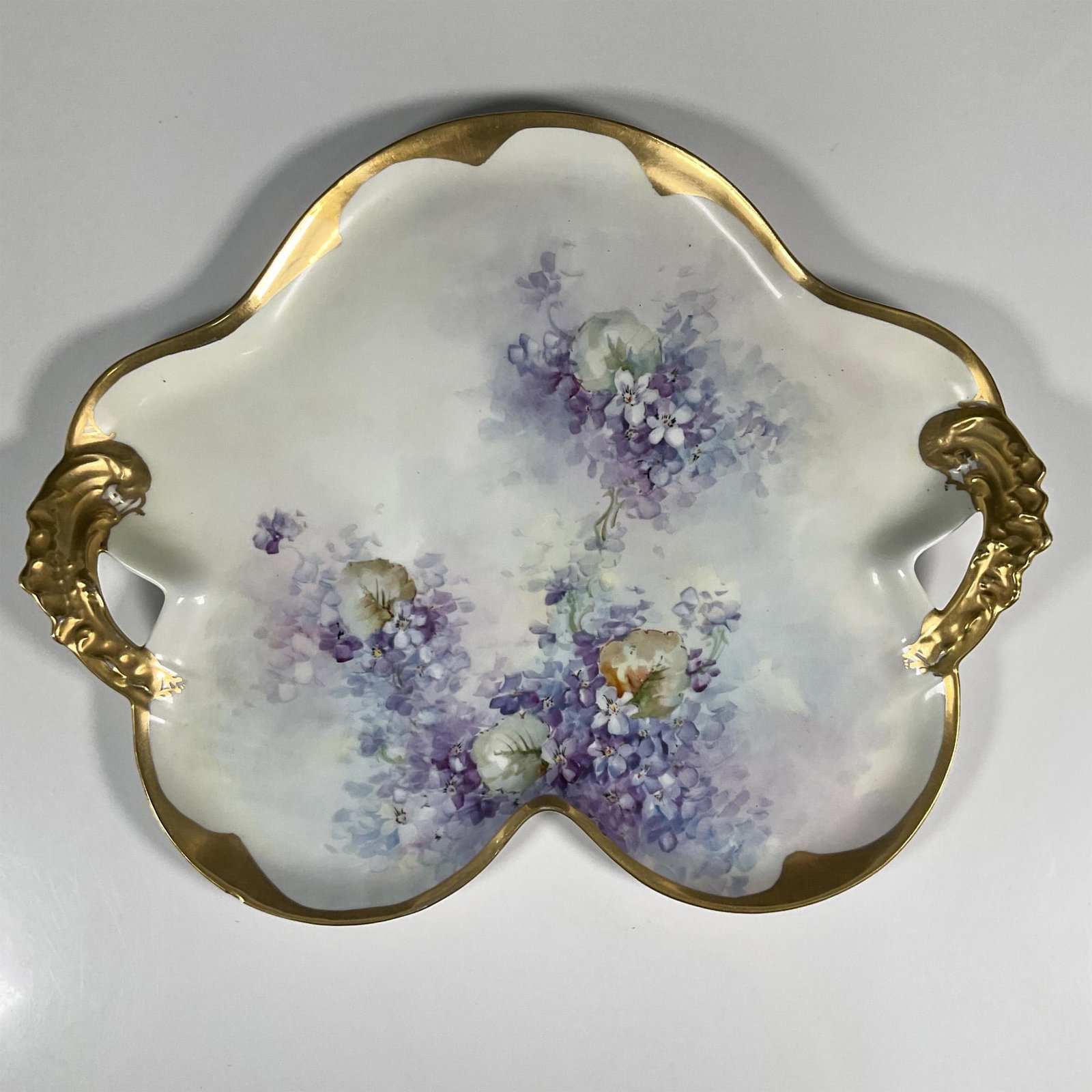 Vintage Porcelain Limoges Floral Centerpiece Tray: A floral shaped tray adored with hand painted violets and gilded handles. Dimensions: 17"L x 14"W x 1.75"H Country of Origin: France