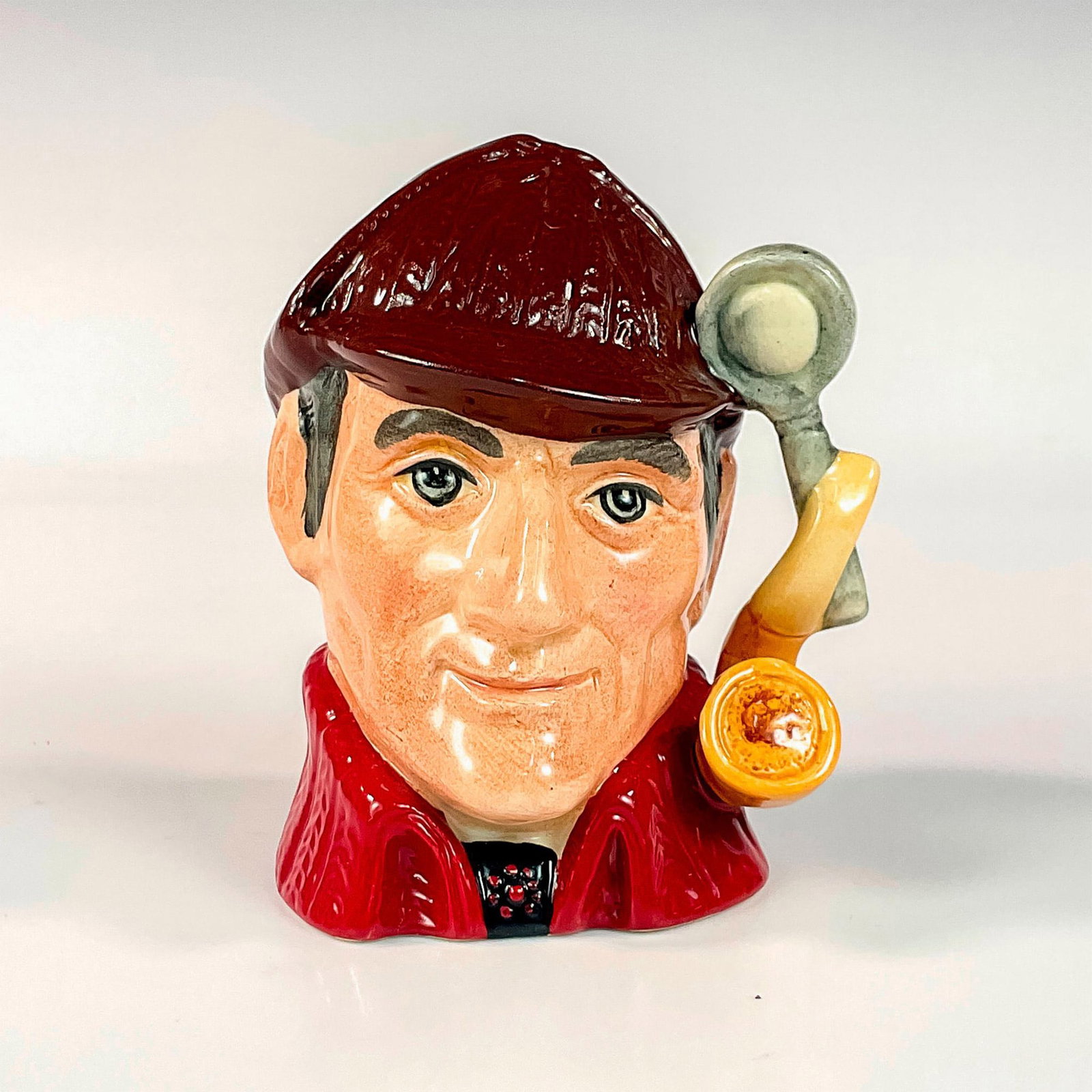 The Sleuth D6773 - Small - Royal Doulton Character Jug: Limited edition of 5000, variation two; brown deerstalker hat and red cloak. Royal Doulton and Lawleys backstamp Issued: 1972 Dimensions: 3â€L x 2.25â€W x 4â€H Manufacturer: Royal Doult