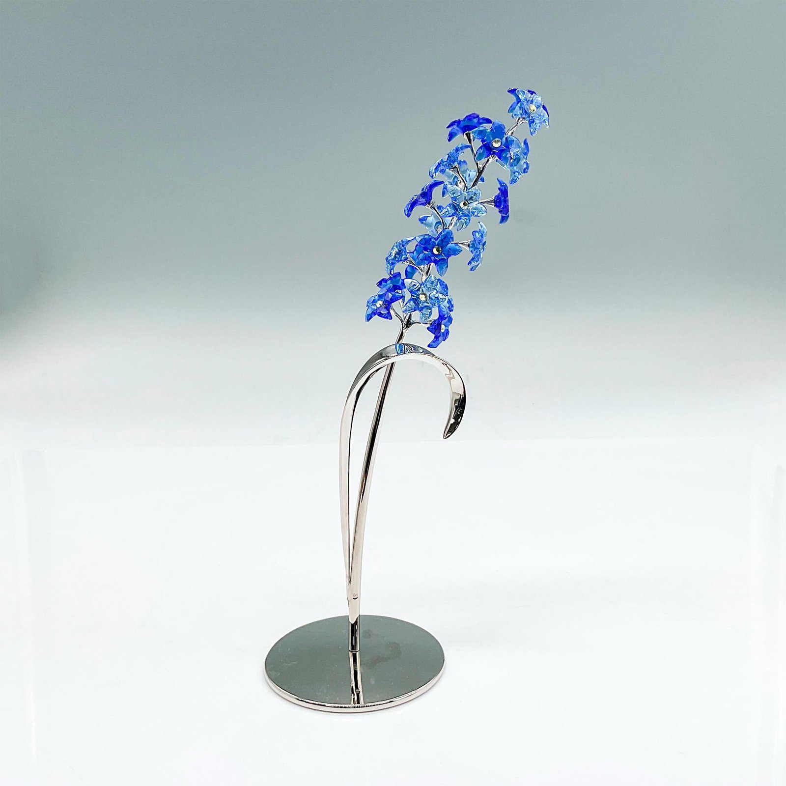 Swarovski Crystal Figurine, Dindori Flowers: Delicate sapphire blue flowers with yellow pistils on a rhodium-plated metal stand. Part of the Exotic Flowers collection. Swarovski backstamp. Includes original box: 12"L x 5.75"W x 4.25"H. Issued: 2