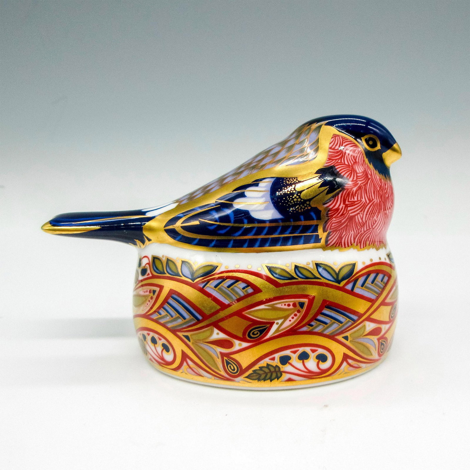 Royal Crown Derby Bone China Paperweight, Bullfinch Nesting: Beautiful bird in dark blue and red coloration with 22k gold accents. Leaves and branch design on nest with same coloration. Royal Crown Derby impressed stopper and backstamp. LXI. Issued: 1996 Dimens
