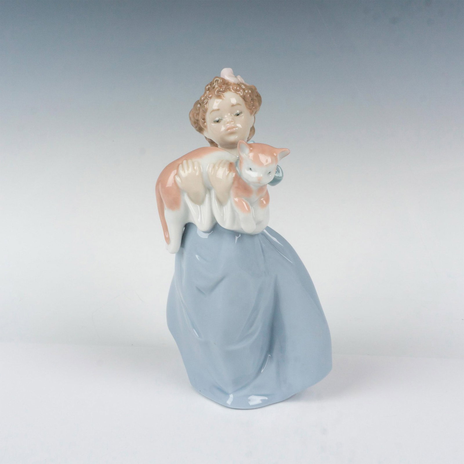 My Chubby Kitty 1006422 - Lladro Porcelain Figurine: Glossy finish; young girl holds her charming kitty with blue bow around his neck. Lladro backstamp. This item has its original box. Box measures: 6.75"L x 11.75"W x 5.5"H. Artist: Francisco Polope Iss