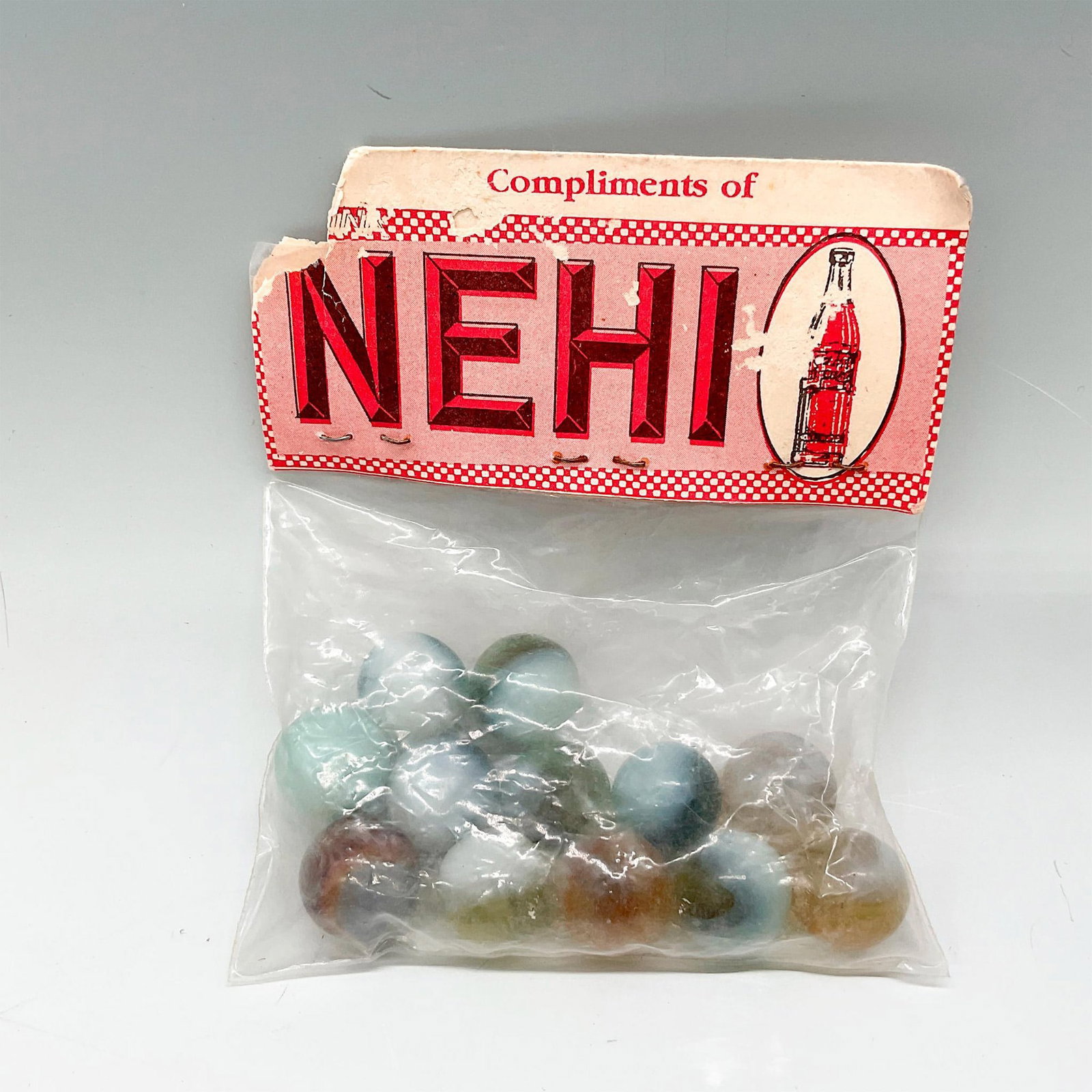 12 Vintage Nehi Marbles: An unopened and original Nehi bag. Contains 12 marbles; white, green, dark blue, and brown coloration. Bag size: 3.5"L x 0.5"W x 4.5"H. Issued: 20th century Manufacturer: Nehi