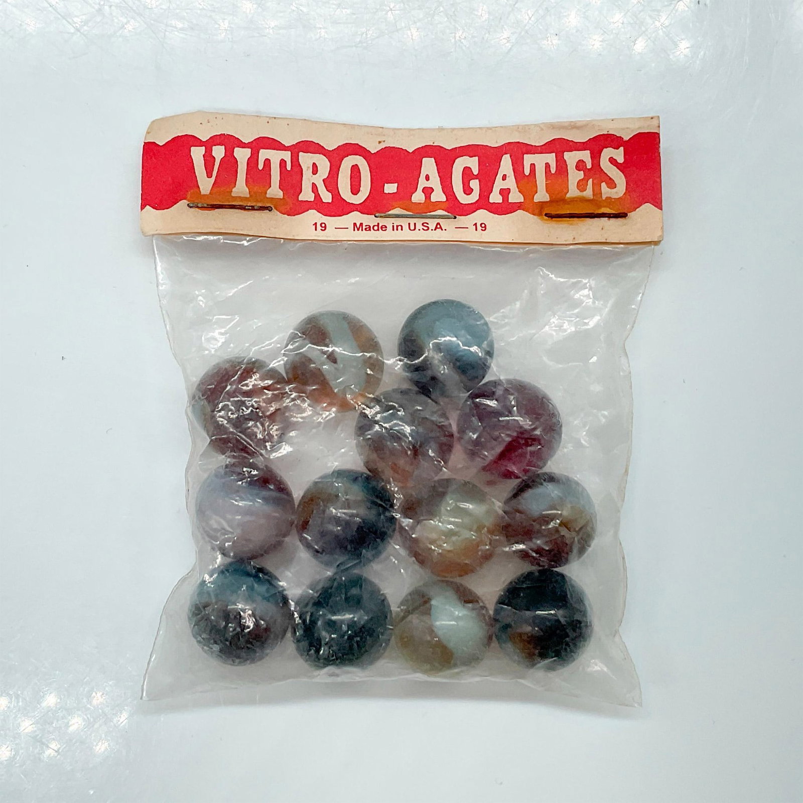 13 Vintage Vitro Agates Marbles: An unopened and original Vitro Agates bag. Contains 13 marbles; brown and amber color hues with white swirls. Bag size: 3"L x 0.5"W x 3.5"H. Issued: 20th century Manufacturer: Vitro-Agates Country of