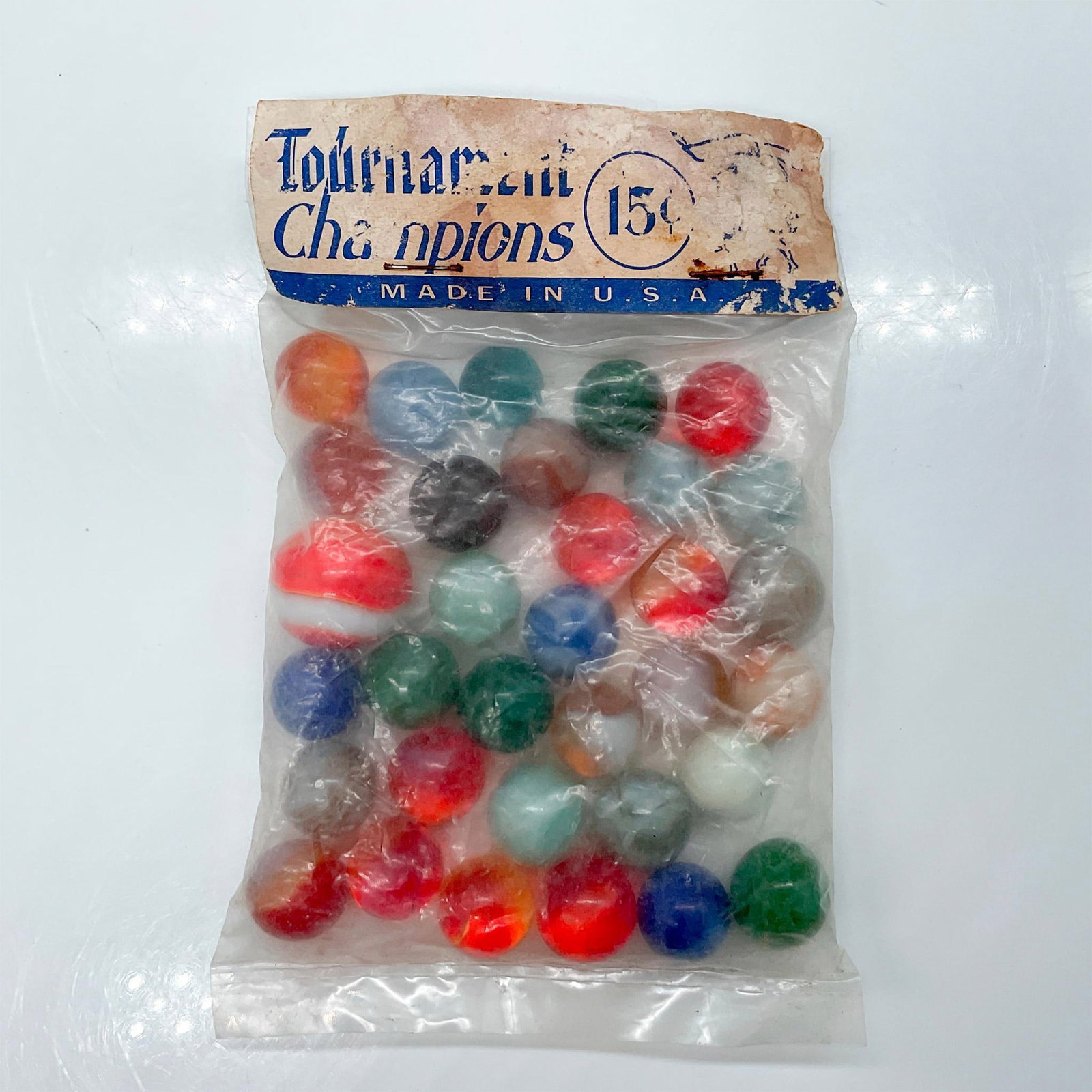 33 Vintage Tournament Champions Marbles: An unopened and original Tournament Champions bag. Contains 32 marbles and 1 shooter; orange, blue, green, yellow, red, and white coloration. Bag size: 4"L x 0.75"W x 6"H. Issued: 20th century Country