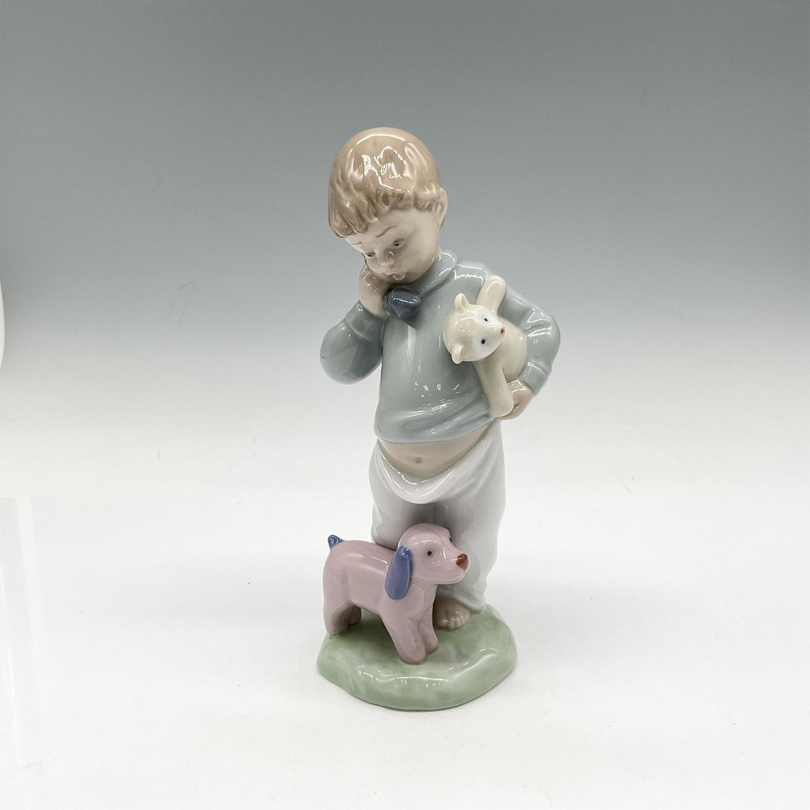 Nao by Lladro Porcelain Figurine, Boy on Phone with Puppets: Glossy adorable figural on phone holding his teddy bear. Colored in blue, white and grey. Nao backstamp. Artist: Regino Torrijos Issued: c. 1992 Dimensions: 2.75"L x 2.5"W x 7.5"H Manufacturer: Nao by