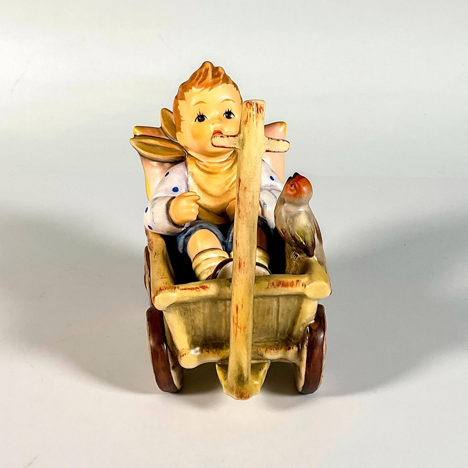 Goebel Hummel Figurine, I'm Carefree: Hand painted in matte finish. Young boy delightfully sits in a wagon, accompanied by a small bird. 1994 first issue. Goebel backstamp. This item has its original box. Box measures: 7.75"L x 7.75"W x 5