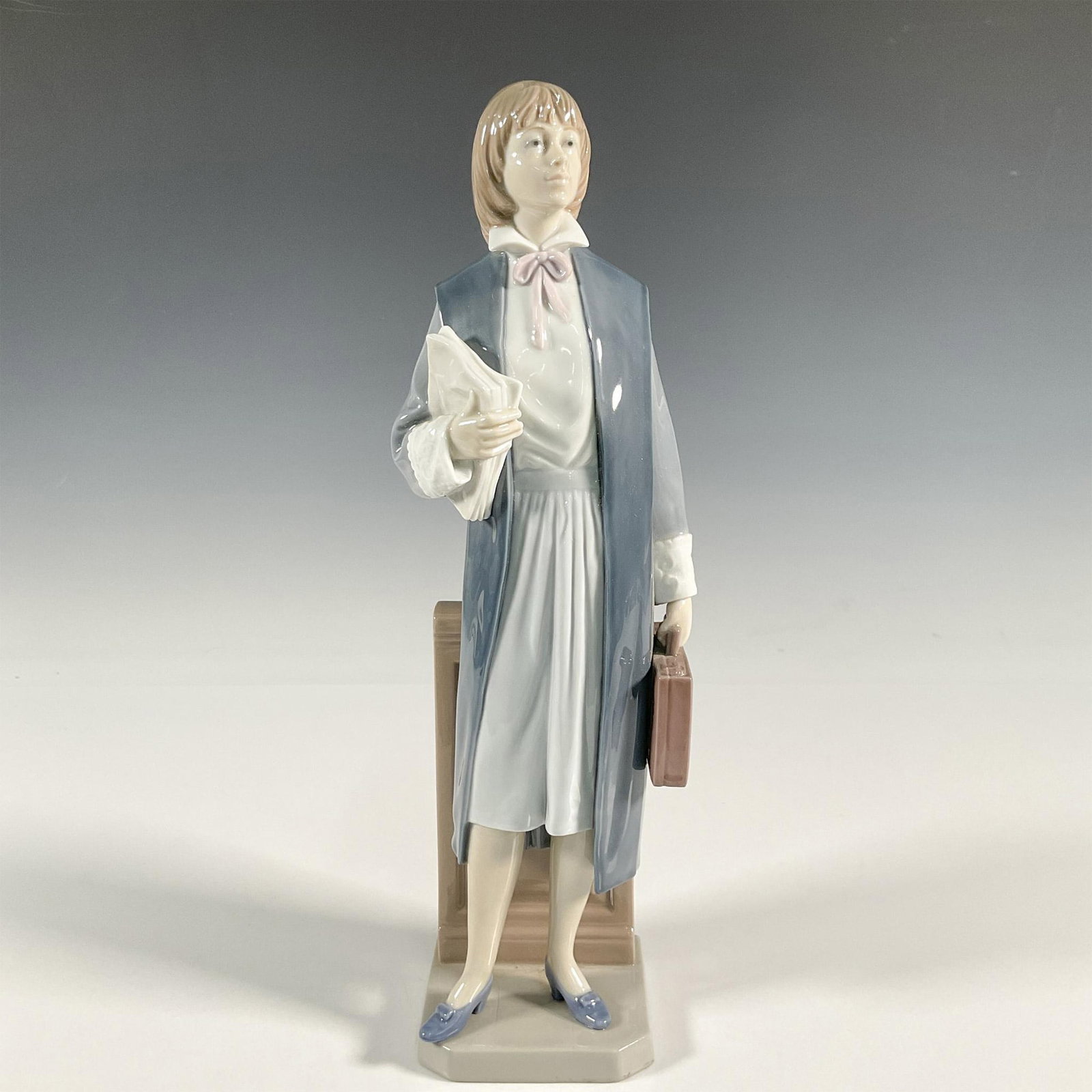 Female Attorney 1006425 - Lladro Porcelain Figurine: A glossy figure of a young lawyer holding a briefcase and a stack of papers. Lladro backstamp. This item has its original box: 17"L x 6.75"W x 6.5"H. Artist: Salvador Furio Issued: 1997-2000 Dimension