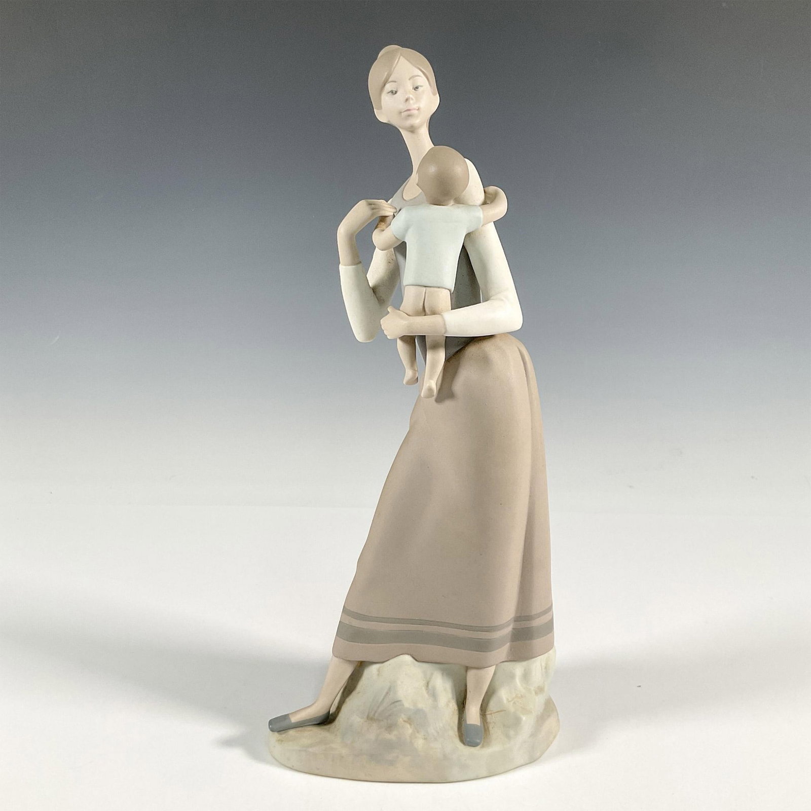 Mother and Child 1014701 - Lladro Porcelain Figurine: A matte figure of a mother holding her child. Lladro backstamp. This item has its original box: 16"L x 6.5"W x 6.5"H. Artist: Alfredo Ruiz Issued: 1970-1991 Dimensions: 6"L x 4.25"W x 13"H Manufacture