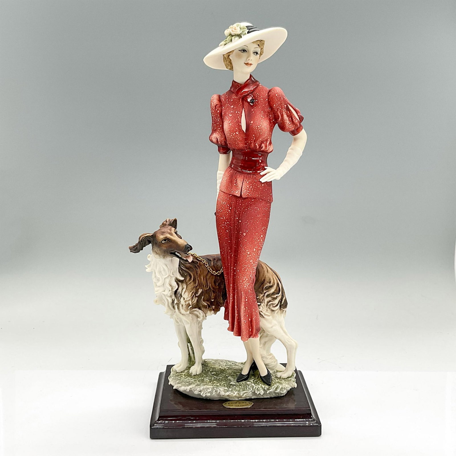 Florence Sculture d'Arte Giuseppe Armani Figurine, Natasha: Cream color matte figure of a sharply dressed lady in a red suit and wide brimmed hat with her dog standing next to her. Florence Sculture d'Arte affixed label. Artist: Giuseppe Armani Issued: c. 1997