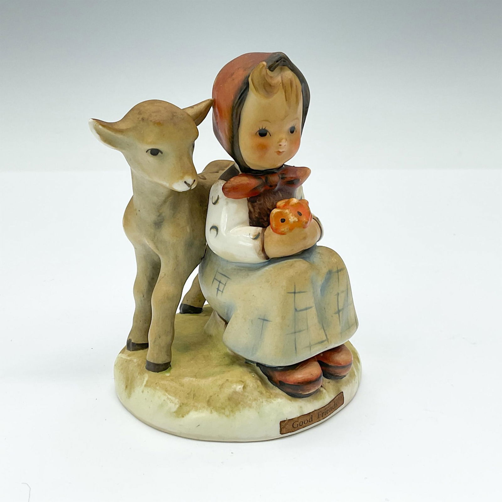 Good Friends HUM182 - Goebel Hummel Figurine: Hand-painted porcelain figurine depicting a farm girl seated, holding flowers, with her lamb friend keeping her company. Goebel TMK3. Issued: 1960-1972 Dimensions: 3.25"L x 3"W x 4"H Manufacturer: Goe