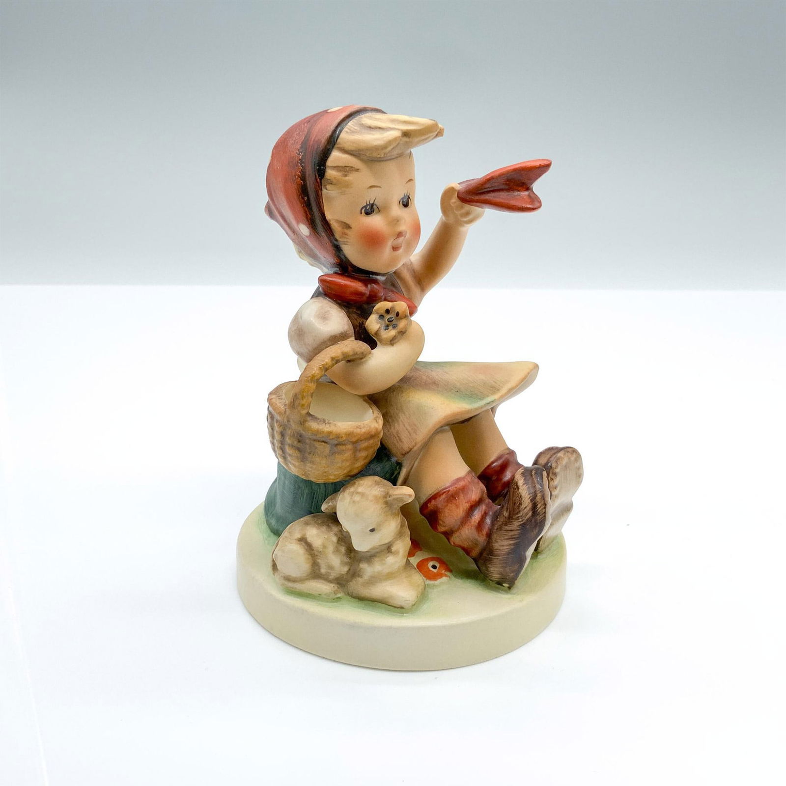 Farewell 65 - Goebel Hummel Figurine: Hand-painted figurine depicting a girl sitting with a lamb and waving a handkerchief. Goebel backstamp on the bottom. Dimensions: 3.5"dia. x 5"H Manufacturer: Goebel Hummel Country of Origin: Germany