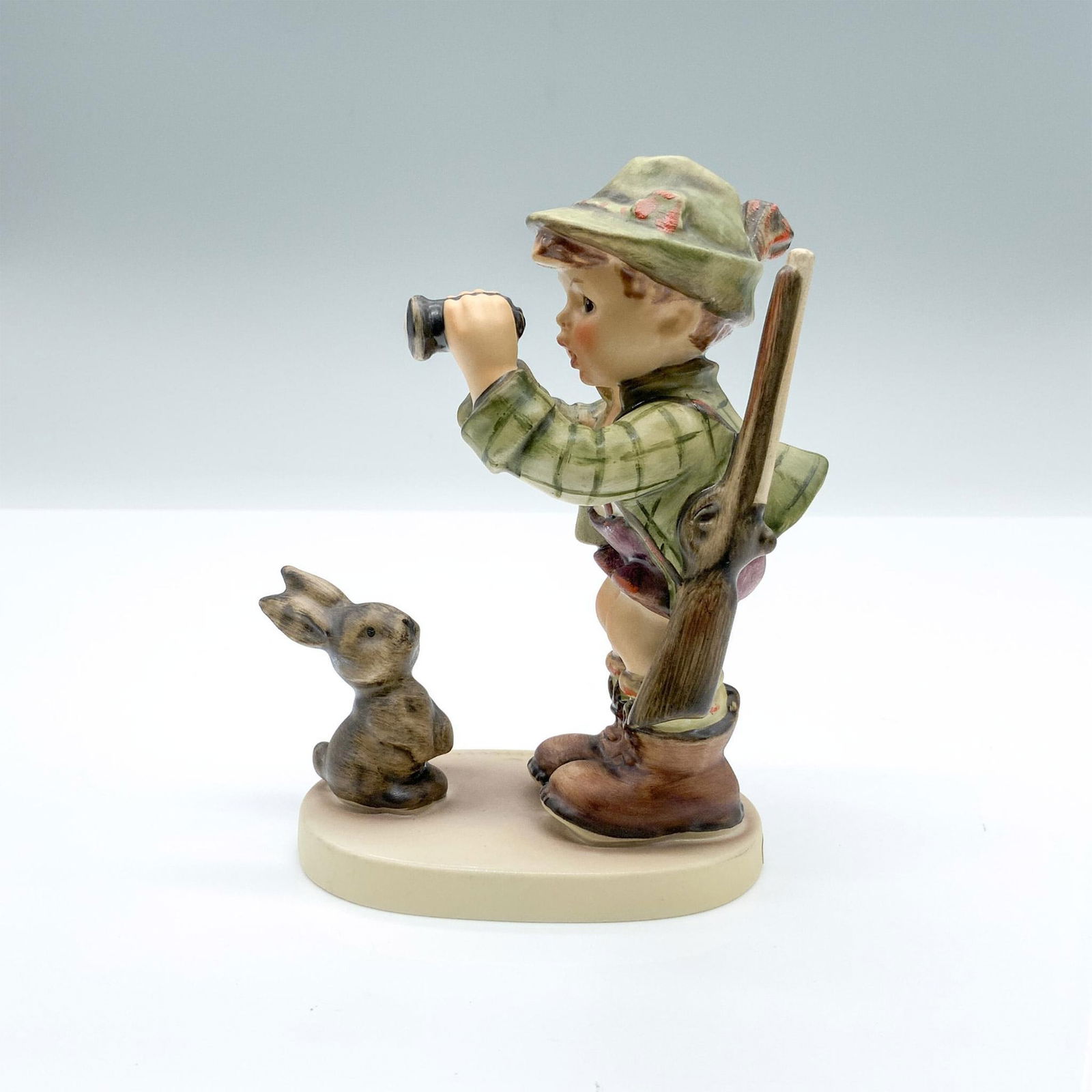 Good Hunting 307 - Goebel Hummel Figurine: Hand-painted figurine depicting a boy holding binoculars and rifle with a bunny right in front of him. Goebel backstamp on the bottom. Dimensions: 3.5"L x 2.25"W x 5"H Manufacturer: Goebel Hummel Coun