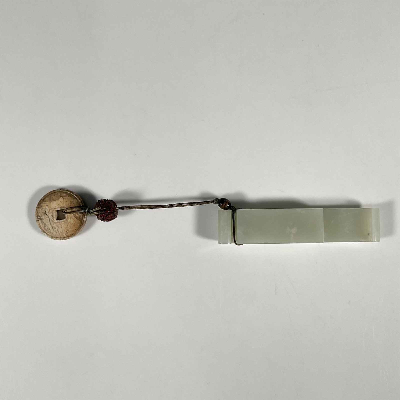 Chinese Ming or Qing Dynasty Jade Sword Belt Accessory: A beautiful carved white jade accessory for a sword belt. A carved nut, and a chicken bone jade coin-like disc dangles from the jade on a green thread. Jade: 0.75"L x 3.75"H x 0.5"D. Nut: 0.5"W x 0.5"