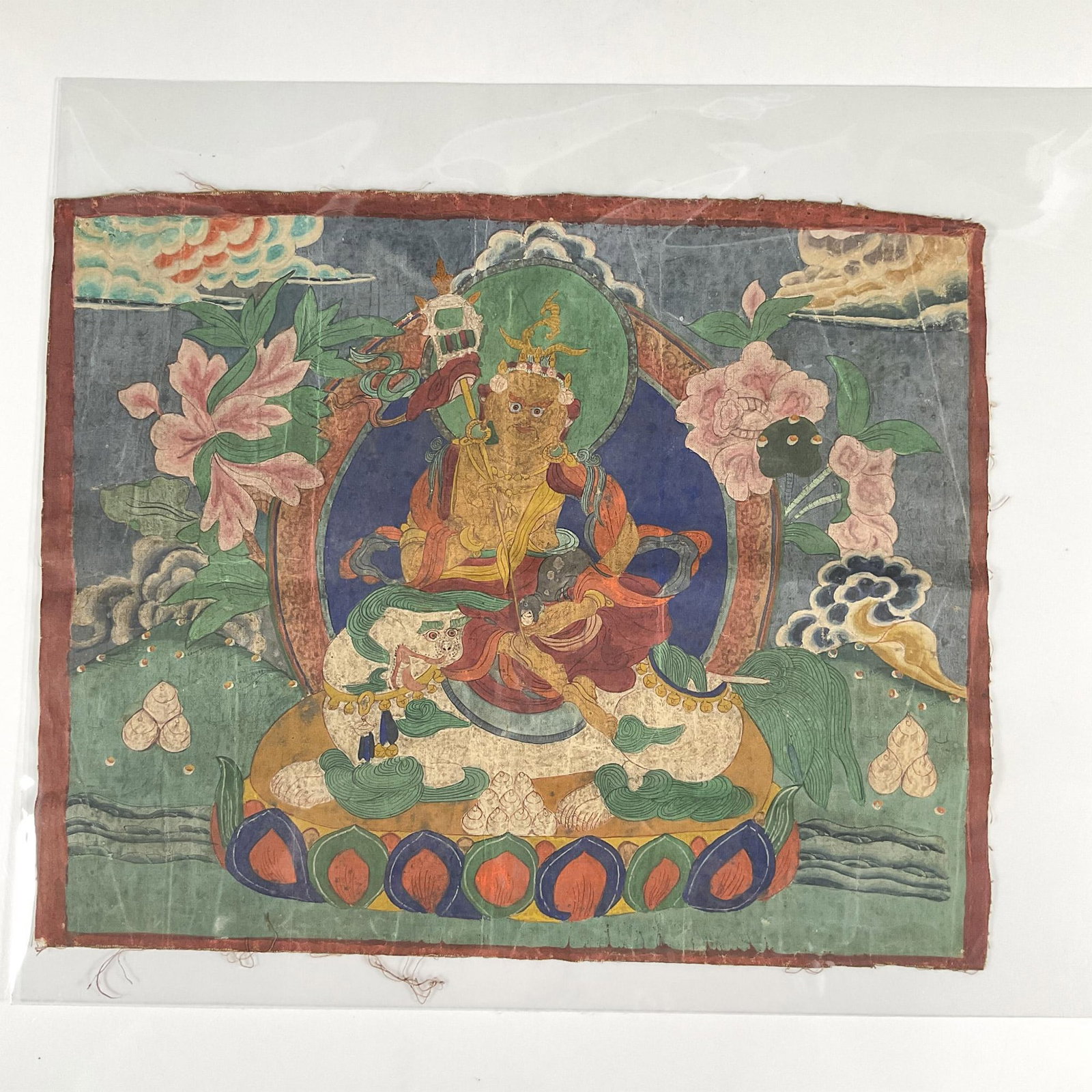 Antique Painting on Canvas of the Tibetan Thangka: A beautiful illustration of the Tibetan Buddhist seated on a beast with clouds and pink blossoms around him. Dimensions: 16.25"W x 13.5"H Country of Origin: China