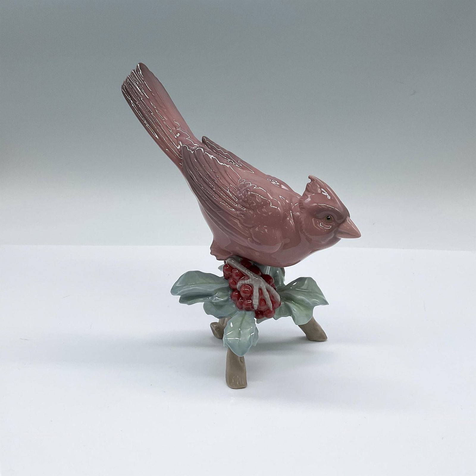 Lladro Porcelain Figurine, Cardinal 1008116: Glossy figure of a red cardinal perched on a holly branch. Lladro backstamp. Artist: Miguel Angel Santaeulalia Issued: 2005-2008 Dimensions: 5.75"L x 3.25"W x 6.5"H Manufacturer: Lladro Country of Or