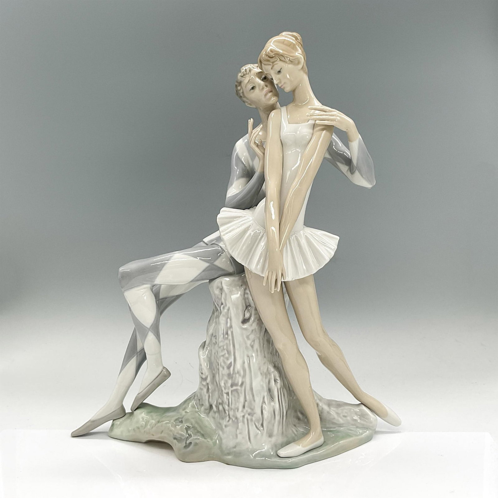 Lladro Porcelain Figure, Idyl, Harlequin & Ballerina 1001017: Glazed porcelain figure of a sitting man with his arms around a standing ballerina lady. Lladro backstamp. Artist: Alfredo Ruiz Issued: 1969-1991 Dimensions: 12"L x 5.5"W x 14.5"H Manufacturer: Lladro