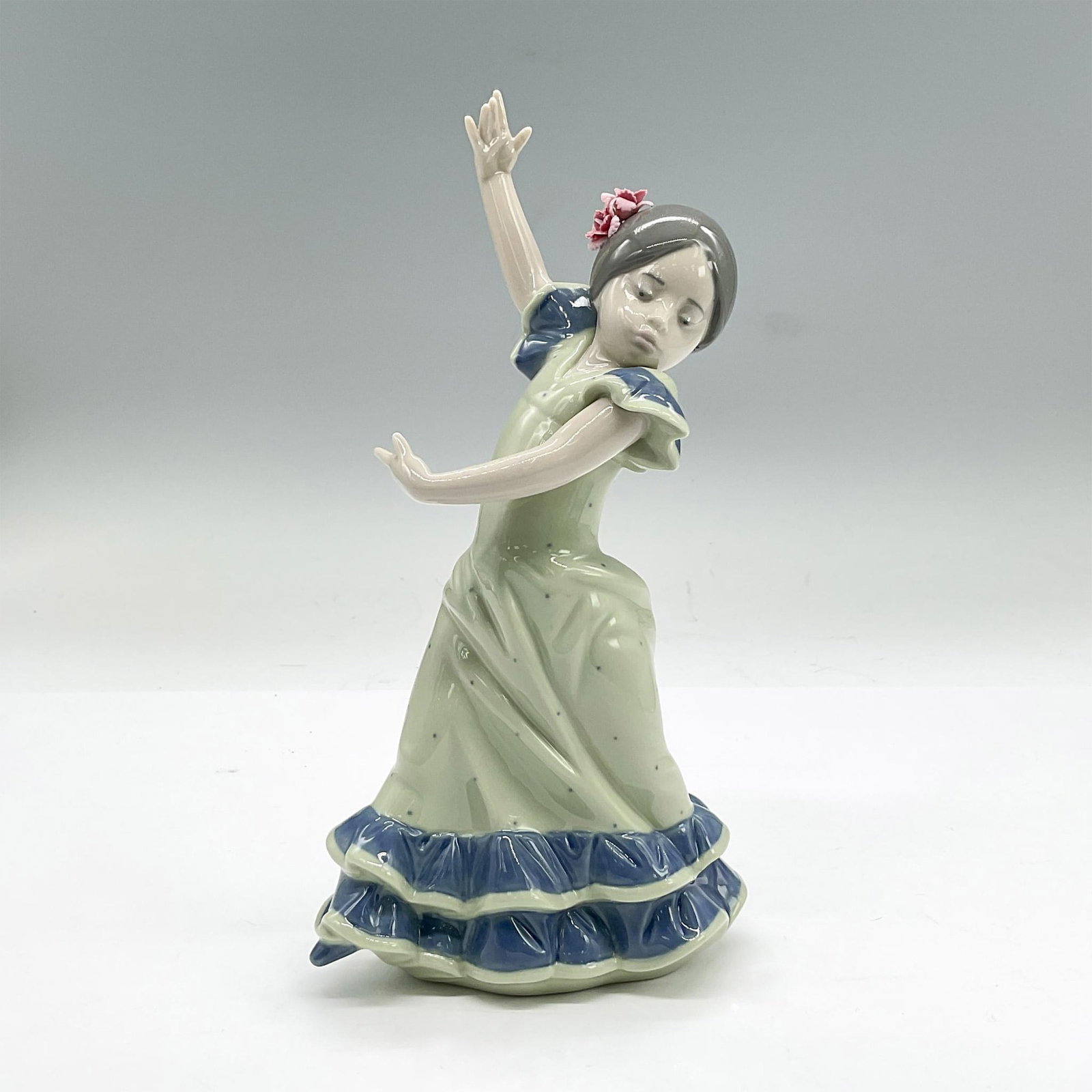 Lladro Porcelain Figurine, Lolita 1005192: Glazed porcelain figure of a young Flamenco dancer girl in a green and blue dress. Lladro backstamp. This item has its original box: 10.5"L x 5.25"W x 4.75"H. Issued: 1984 Dimensions: 4"L x 2.5"W x 7"