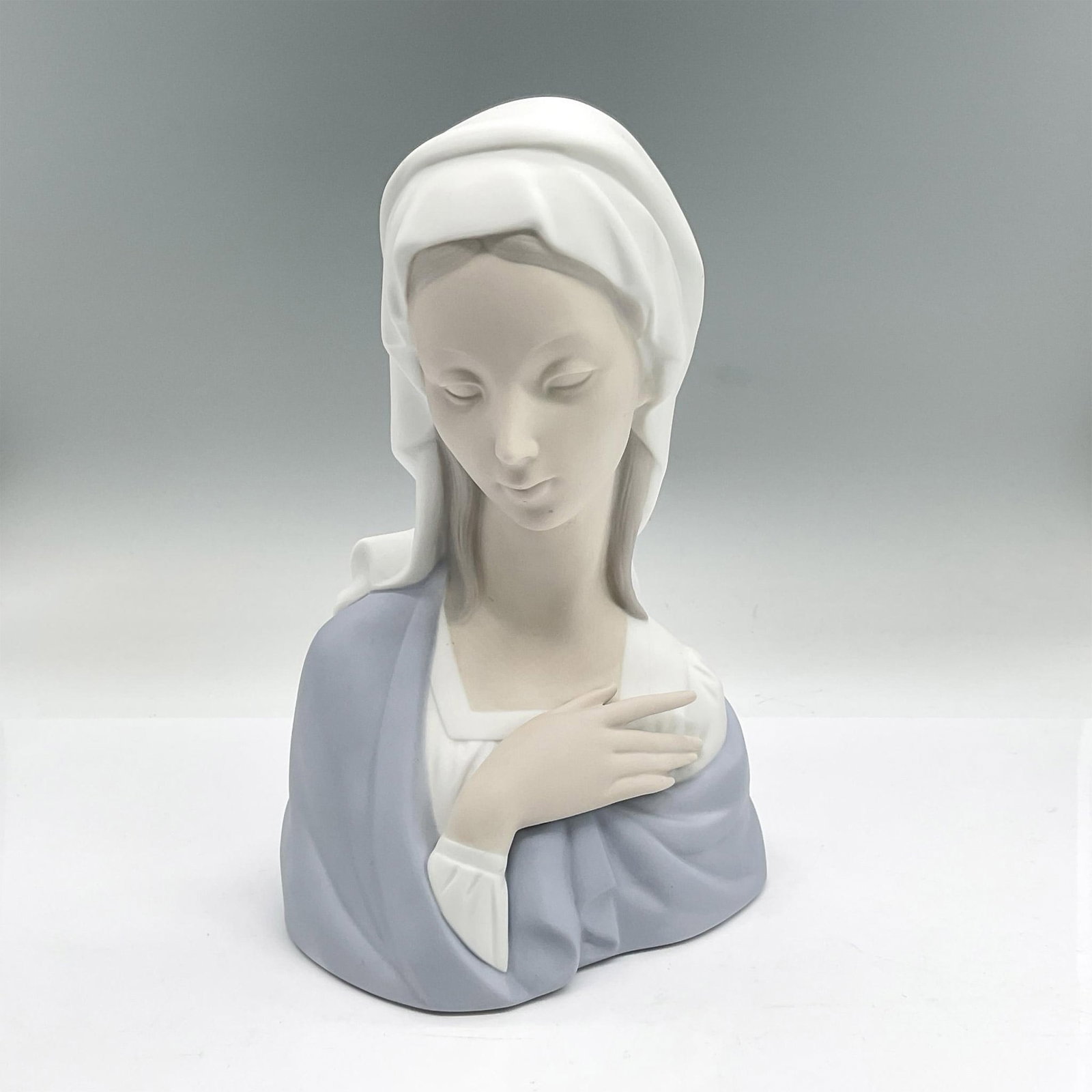 Lladro Porcelain Bust, Madonna Head 1004649: Matte porcelain bust of the iconic Mary in a white headdress and blue shawl. Lladro backstamp. Artist: Vincente Martinez Issued: 1969-2001 Dimensions: 5.5"L x 3.75"W x 8.25"H Manufacturer: Lladro Cou