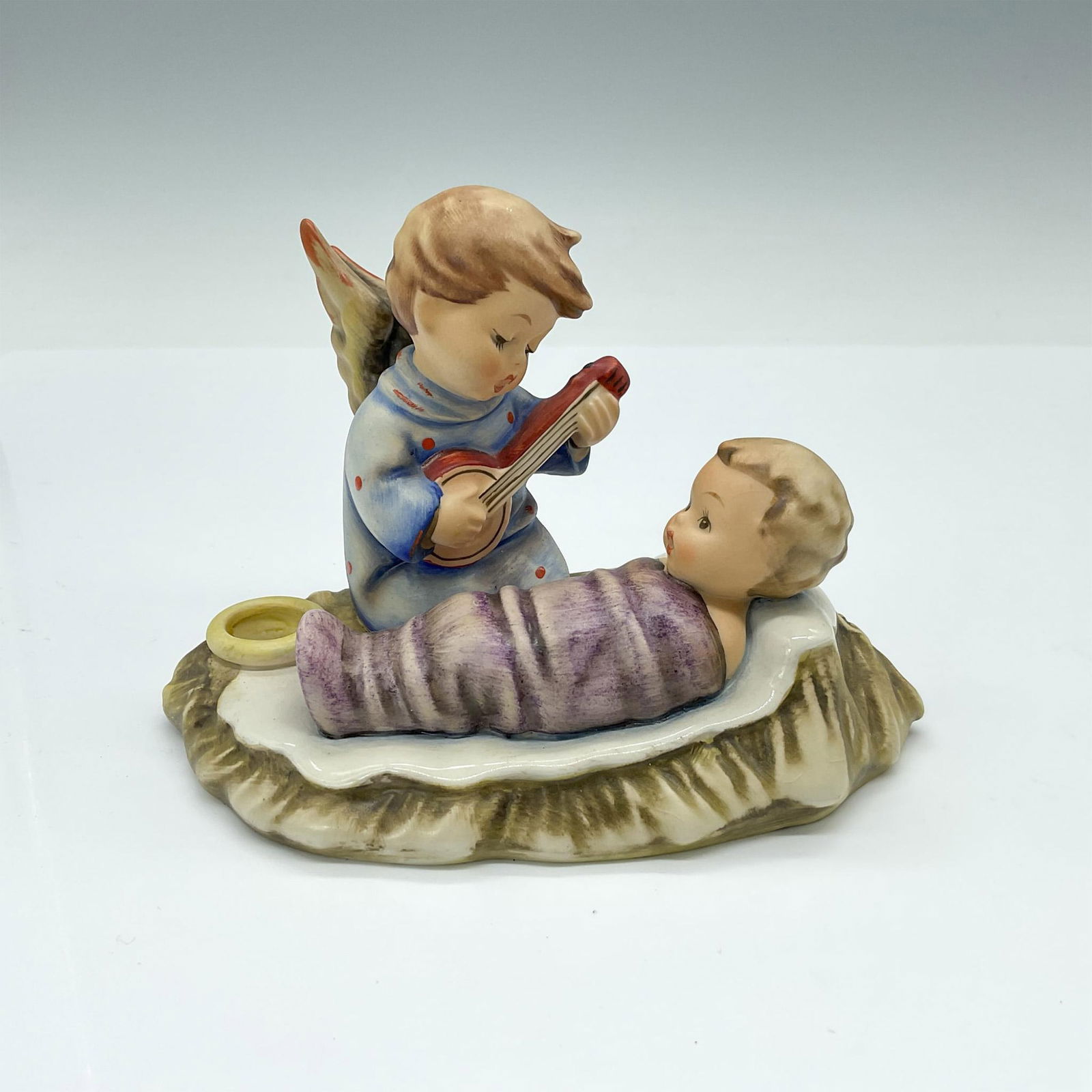 Goebel Hummel Figurine, Lullaby Candle Holder HUM24/I: figurine of little angel in blue dress singing to a baby wrapped in purple blankets. Small candle holder on the side. Goebel TMK5. Issued: 1972-1979 Dimensions: 5.25"L x 3.25"W x 3.5"H Manufacturer: G