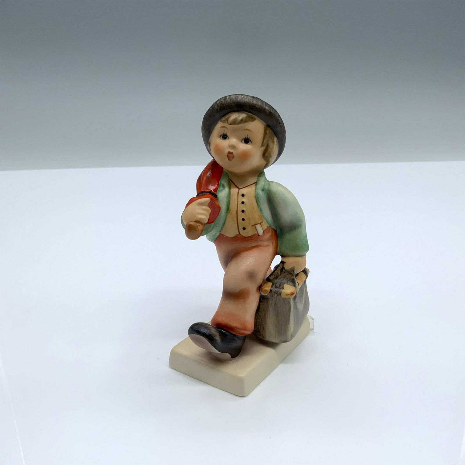 Goebel Hummel Porcelain Figurine, Merry Wanderer 11 2/0: Hand-painted figurine depicting a boy walking with a bag and an umbrella. Goebel backstamp on the bottom. It was a commemorative piece for the 1935 Leipzig Fair. This item has its original box which m