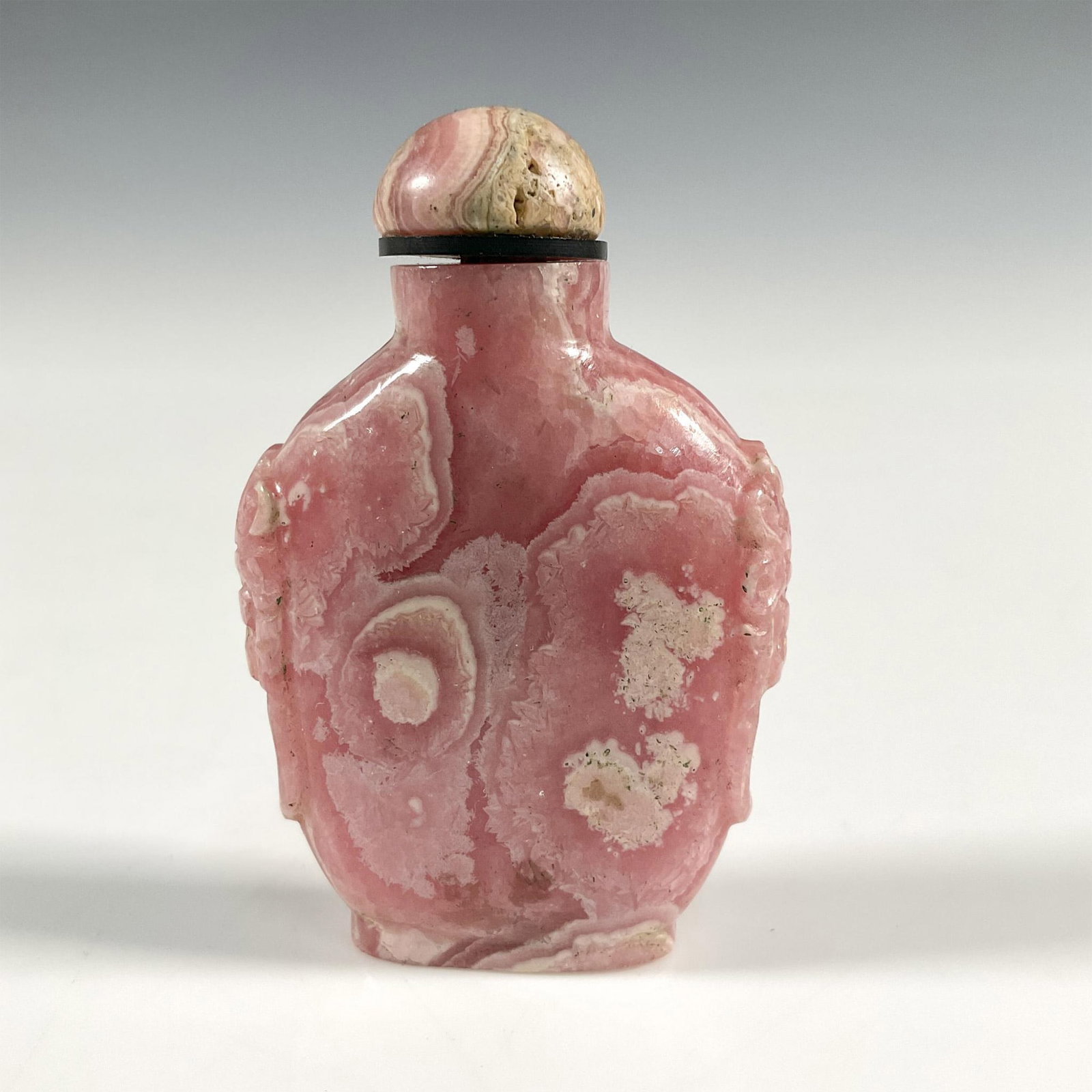 Chinese Rhodochrosite Stone Snuff Bottle: A Chinese carved Rhodochrosite snuff bottle with mythical faces carved on each side, surmounted by rhodochrosite stone conforming stopper. Dimensions: 1.5"L x 0.25"W x 2.25"H