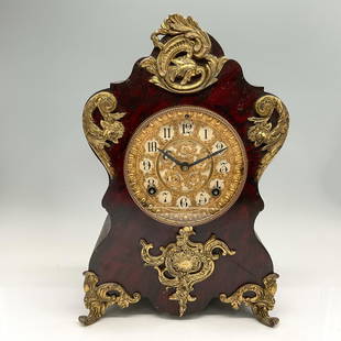 Antique Ansonia Enameled Iron Mantel Clock: Black enameled iron case in late baroque style, decorated with applied gilt brass acanthus ornaments. The round Brass dial behind a glass panel door has Arabic numerals. Ansonia Clock Co. impressed on