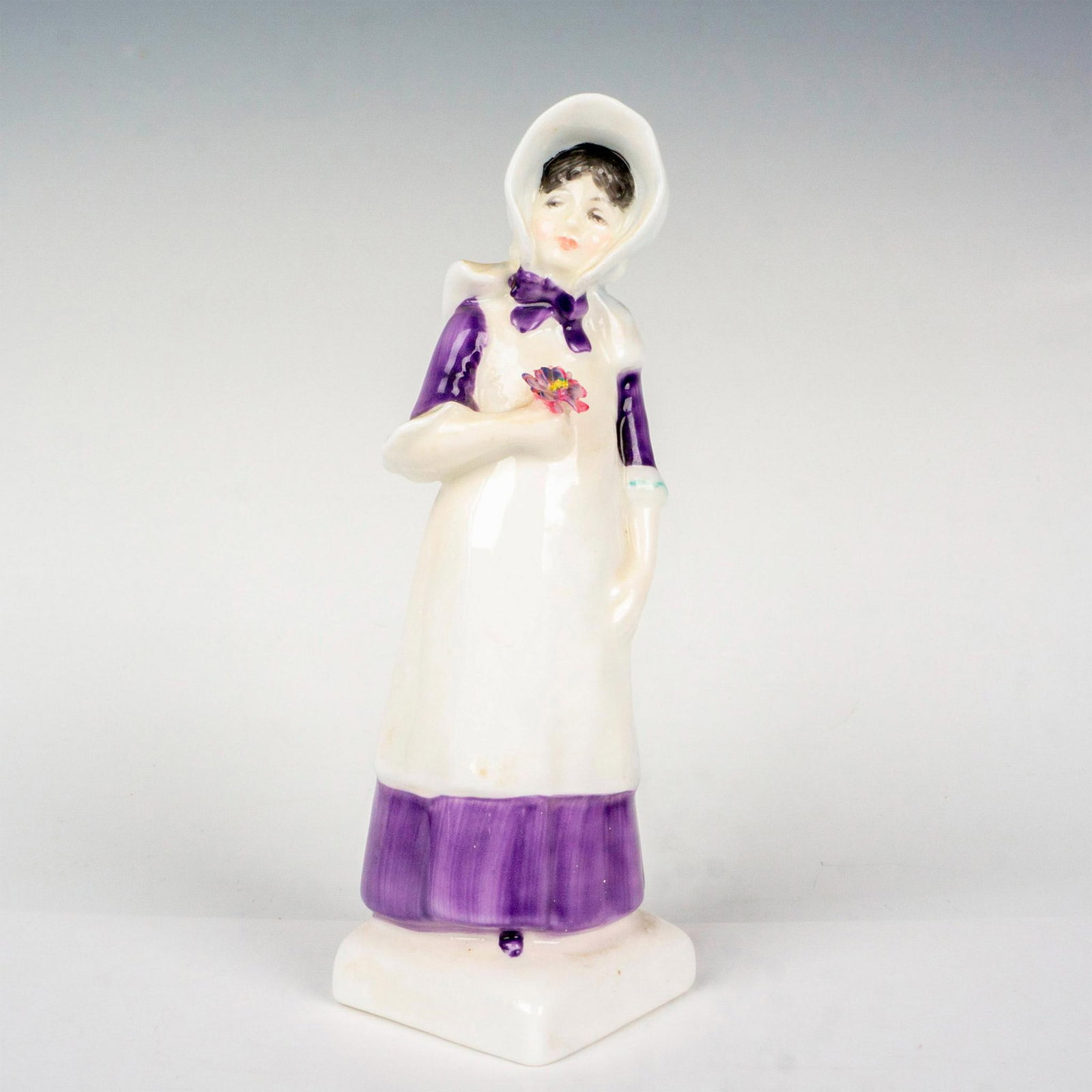 Anna - HN2802 - Royal Doulton Figurine: Glossy finish modeled as young girl in purple gown and apron, holding a single flower. Kate Greenaway series. Royal Doulton backstamp. Artist: Peggy Davies Issued: 1976 - 1982 Dimensions: 5.75"H Manuf