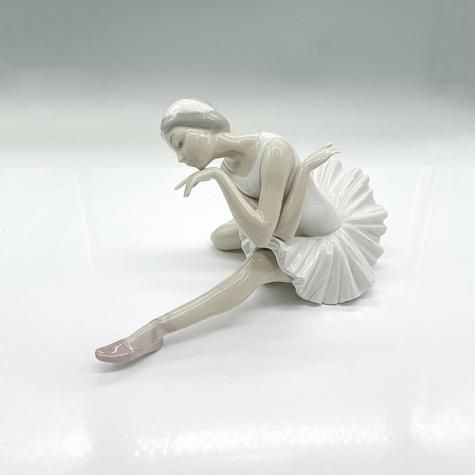 Lladro Porcelain Figurine, Ballerina Death Swan: Porcelain ballerina in a death swan floor pose with crossed arms. Gloss finish. Lladro backstamp. Issued: 20th century Dimensions: 10.25"L x 5.5"W x 5.5"H Manufacturer: Lladro Country of Origin: Spain