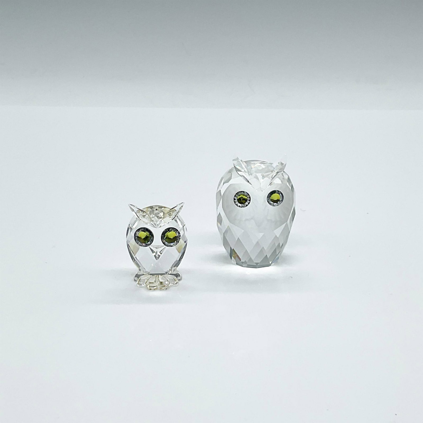 2pc Swarovski Crystal Figurines, Owls: Two cuties. The larger of the two is clear faceted crystal with a frosted face and green crystal eyes. The mini is clear faceted crystal on a flat flower base with green crystal eyes. Swarovski backst