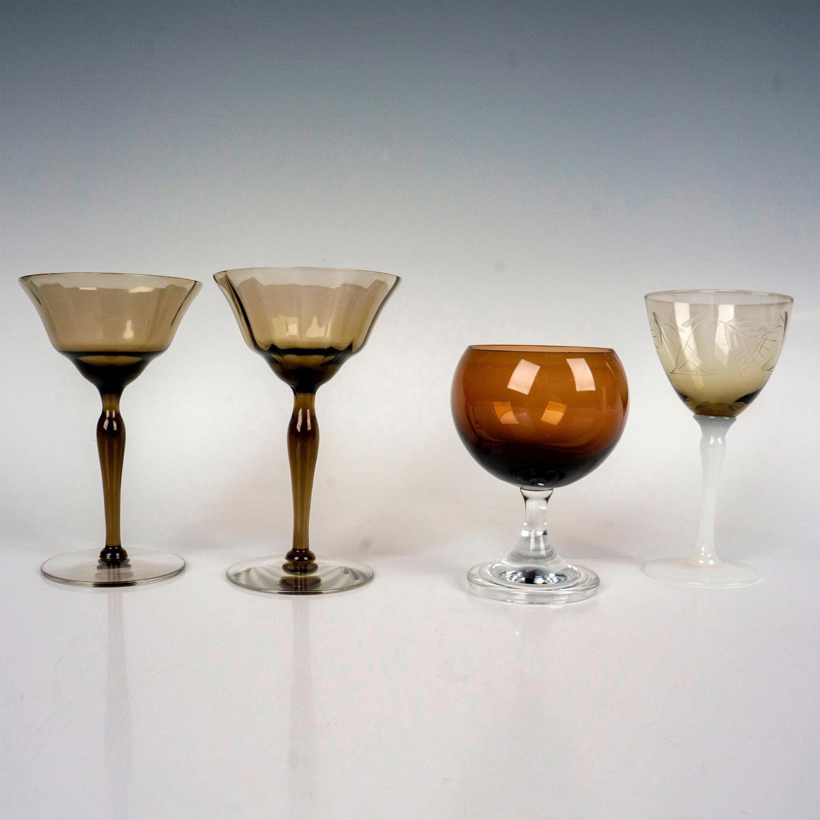4pc Mixed Lot of Drinkware Glasses: Includes 2 brown cordial glasses with clear round base, 1 brown etched glass with white glass stem and 1 Fostoria brandy glass with clear stem and base. Largest piece: 5.5"H x 3.5"dia. Issued: 20th ce