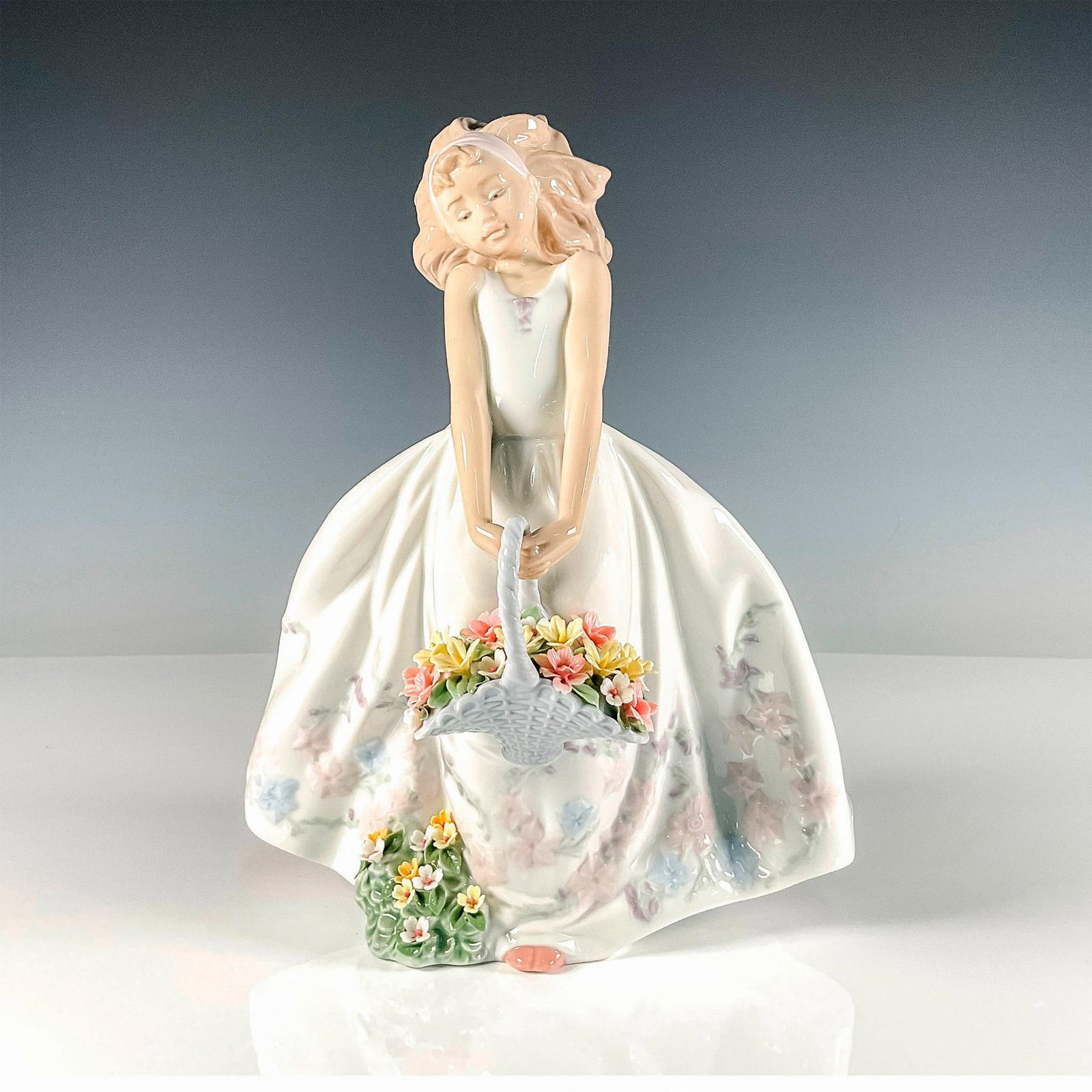 Wildflowers 1006647 - Lladro Porcelain Figurine: Glossy finish figure of a girl with a basket of wildflowers wearing a white dress that is decorated with soft floral ornaments. Lladro backstamp. Artist: Regino Torrijos Issued: 1999 Dimensions: 8"L x