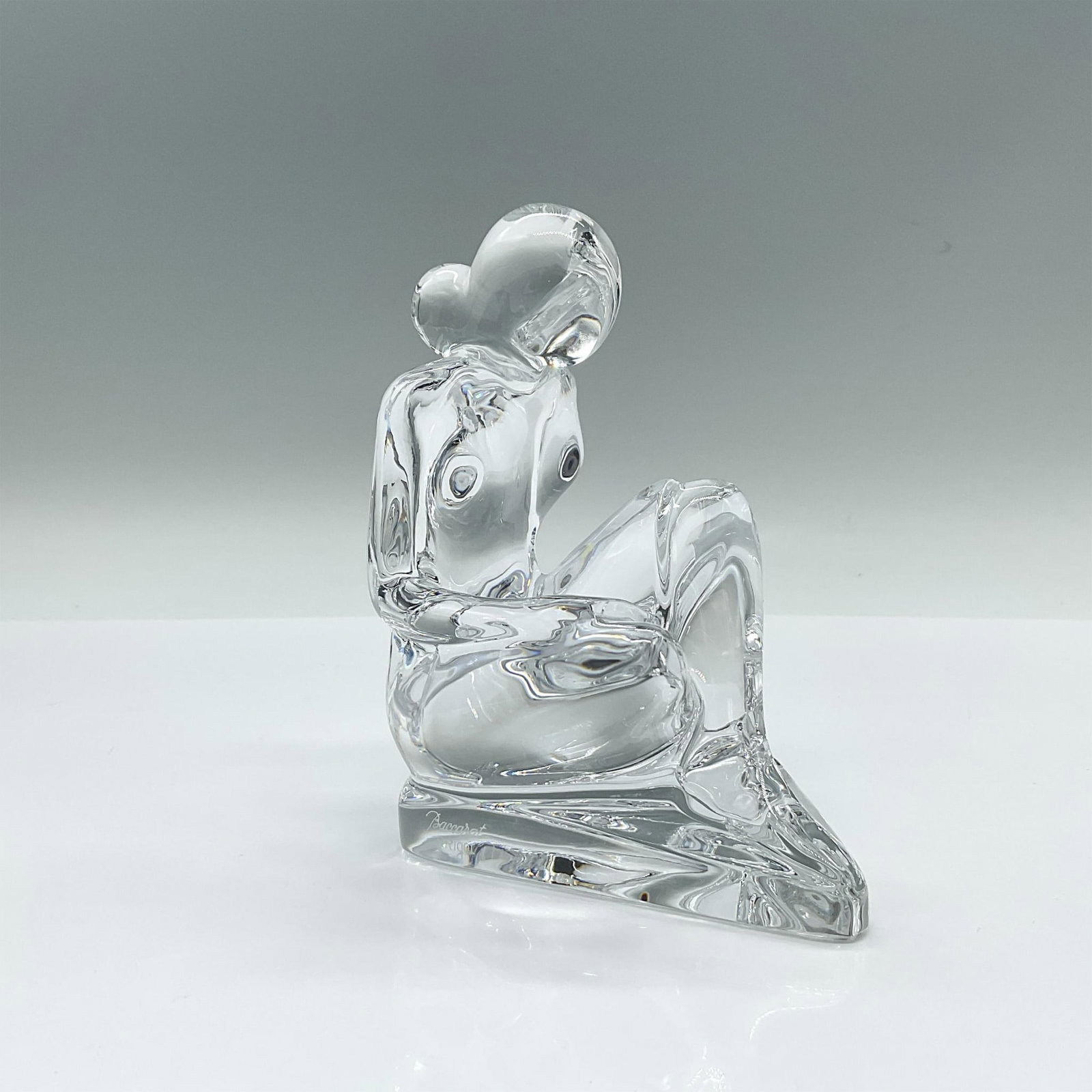 Baccarat Rigot Crystal Nude Figurine: A clear figure of a nude woman reading a large book on her lap. Baccarat Rigot marked on the side. Artist: R. Rigot Dimensions: 5"L x 3"W x 5"H Manufacturer: Baccarat Country of Origin: France