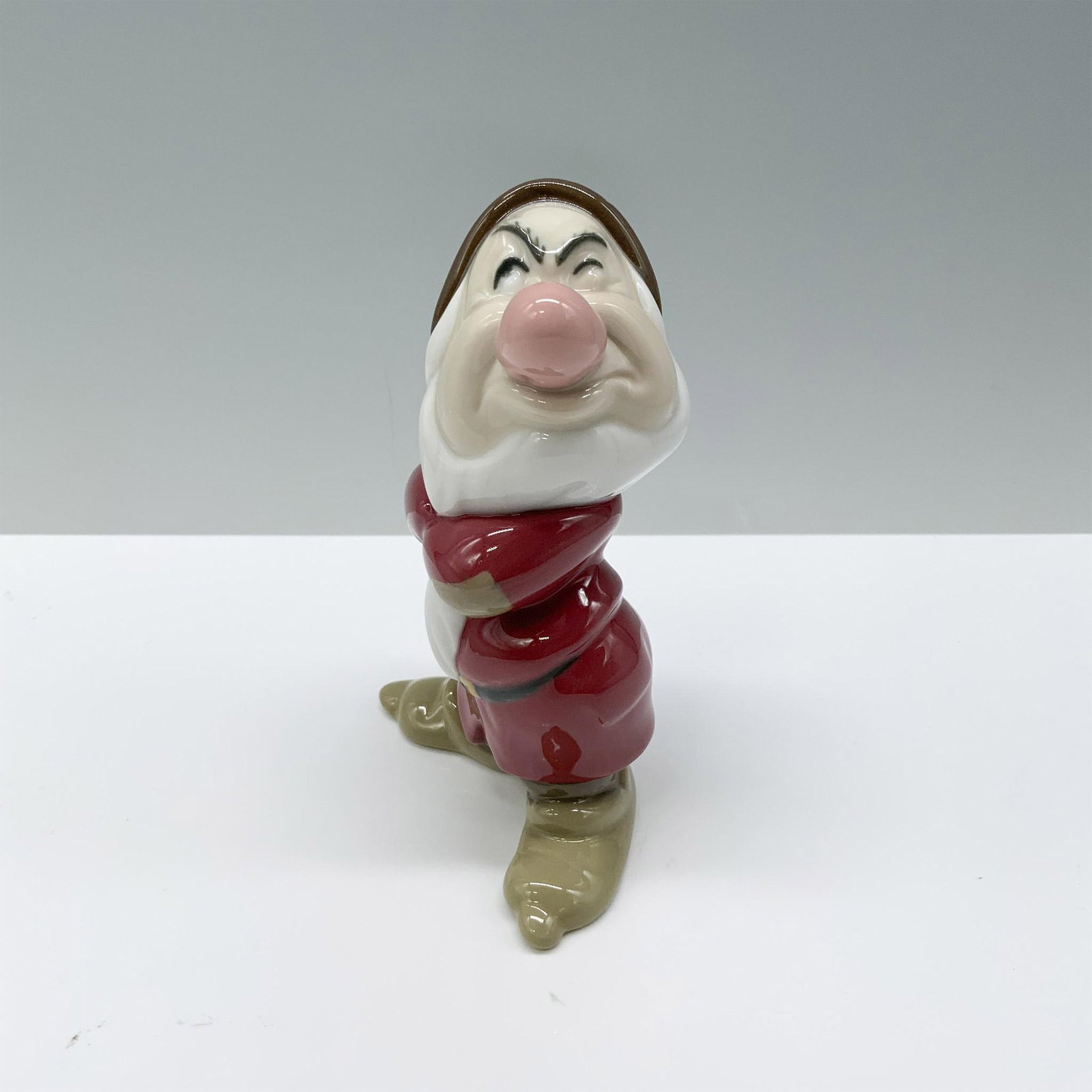 Nao by Lladro Porcelain Disney Figurine, Grumpy: A figurine of Grumpy from Snow White that features him in his traditional outfit, arms crossed and sporting a sour expression. Nao by Lladro backstamp. Artist: Eva Maria Cuerva Issued: 2014 Dimensions