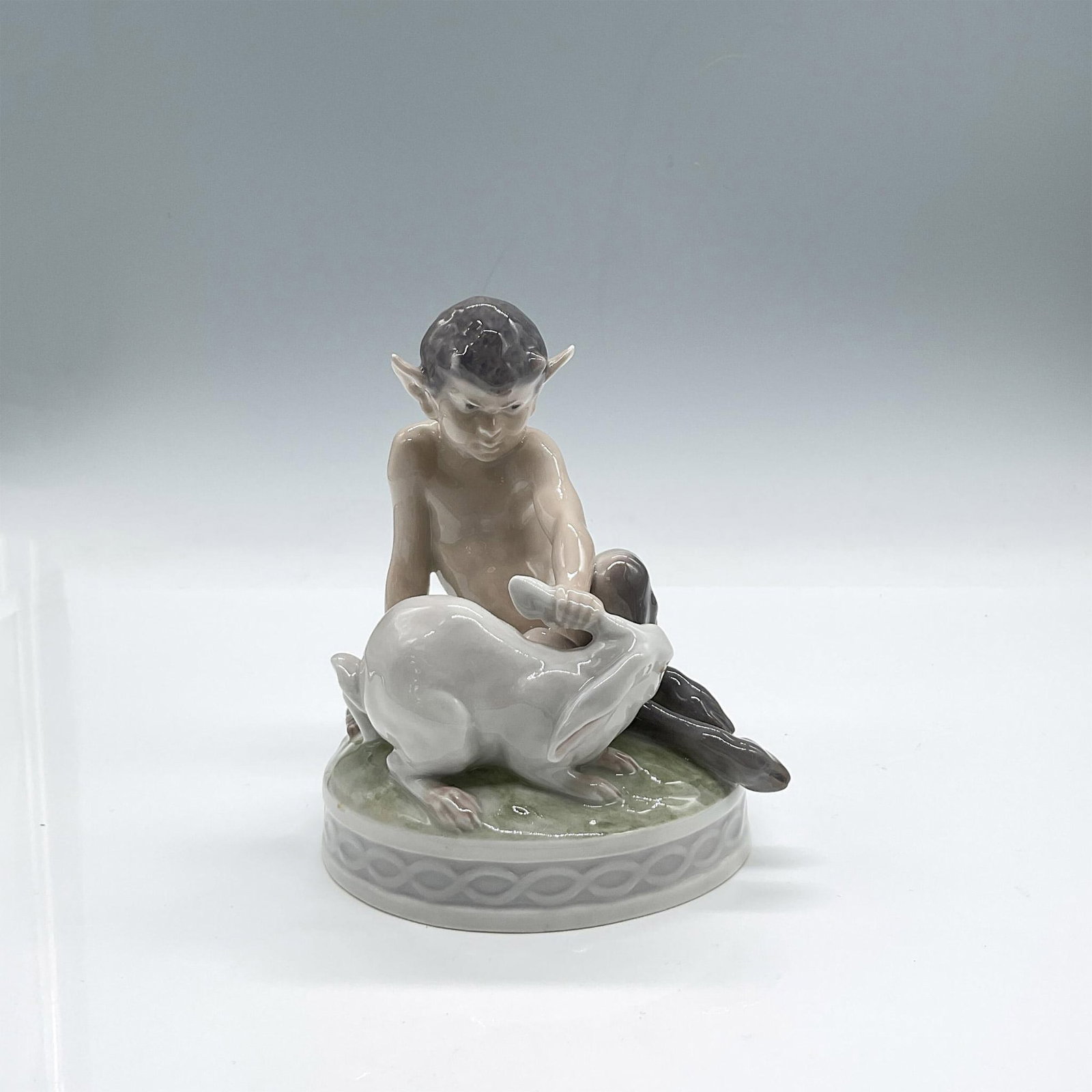 Royal Copenhagen Figurine, Faun and Rabbit, 439: Charming porcelain figure of a faun resting one hand on his flute and the other tugging a rabbit's ear. Glossy finish. Royal Copenhagen backstamp. Issued: 1968 Dimensions: 4.50"L x 4.25"W x 5"H Manufa